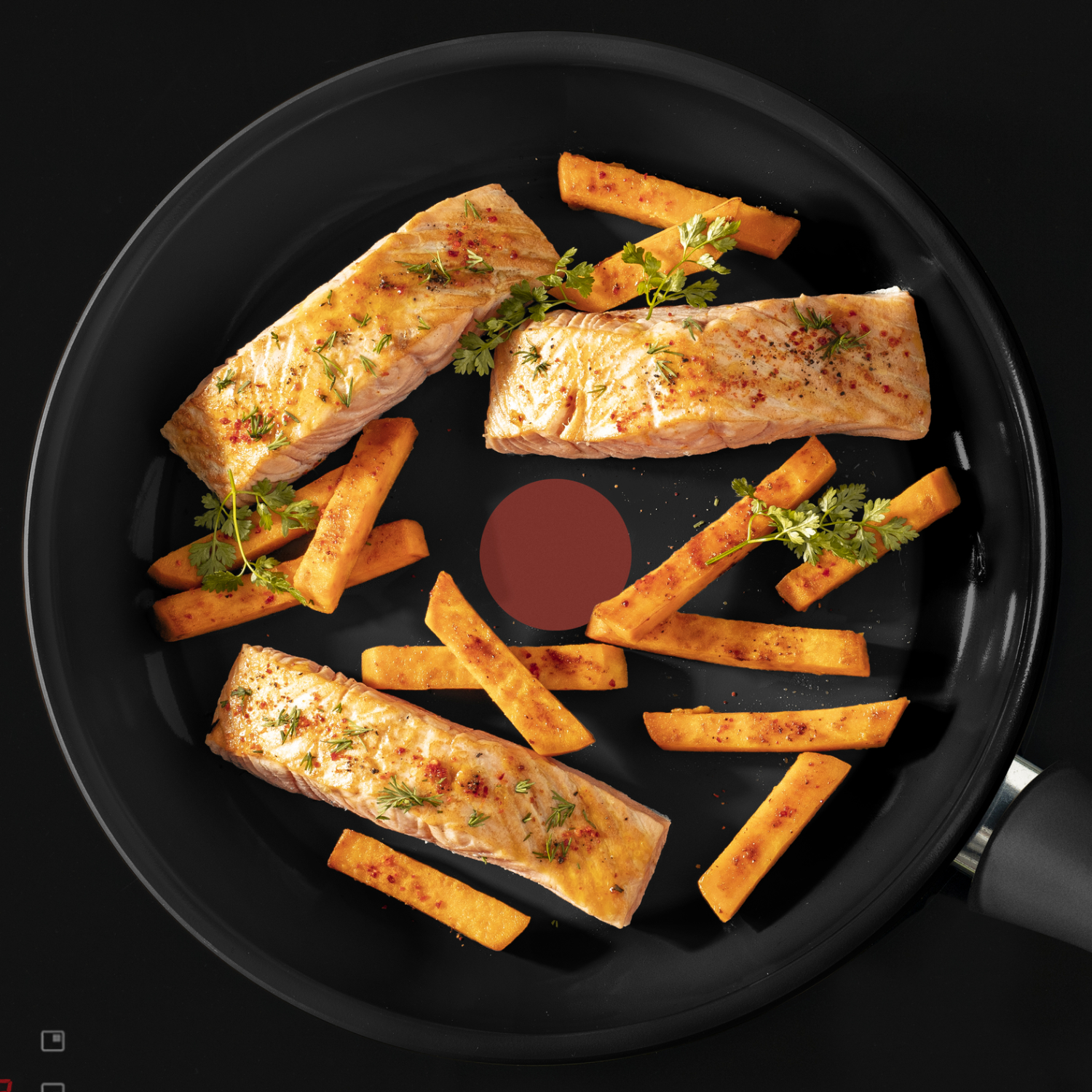 Een pan met zalm en zoete aardappelfriet, gegarneerd met peterselie, op een zwart oppervlak.