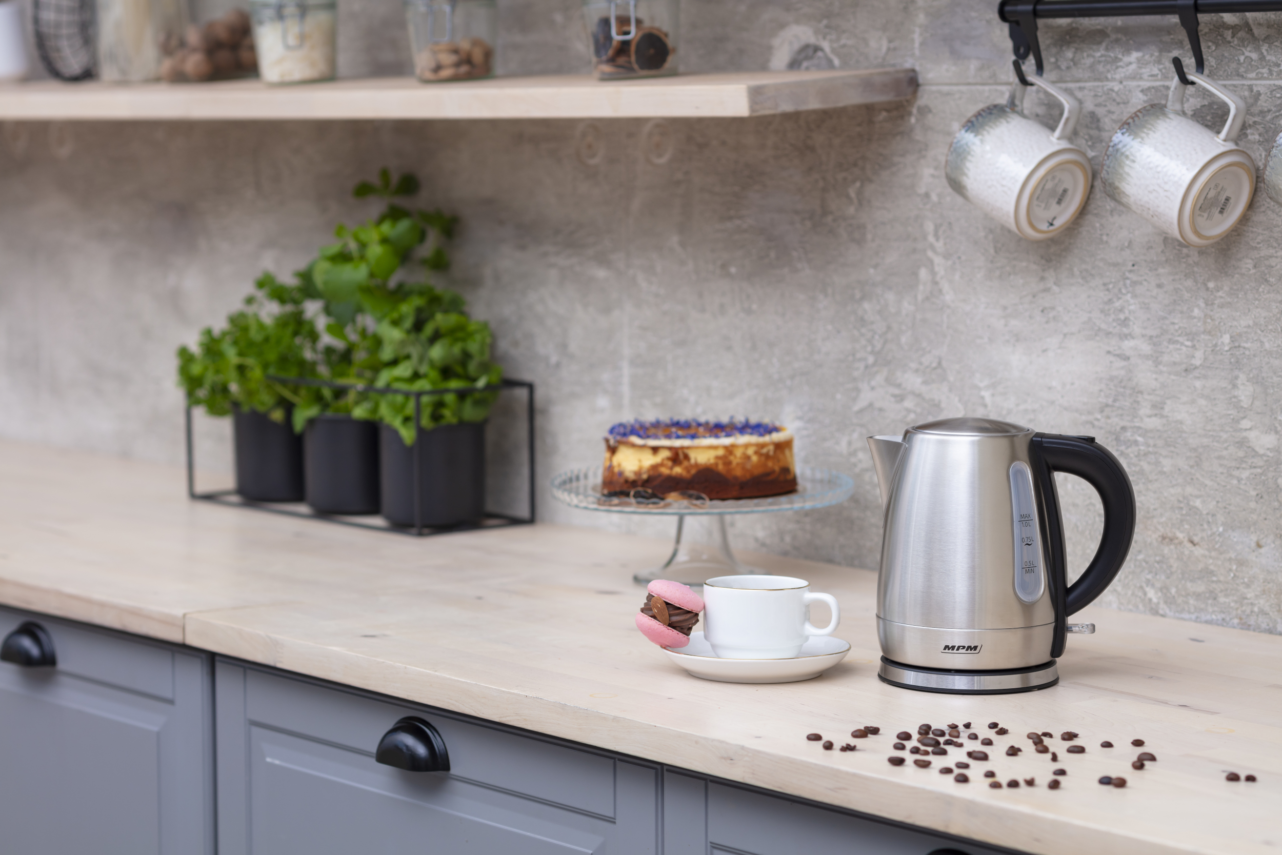 Blat kuchenny z czajnikiem, ciastem, makaronikiem i ziarnami kawy. Widoczne rośliny i kubki.