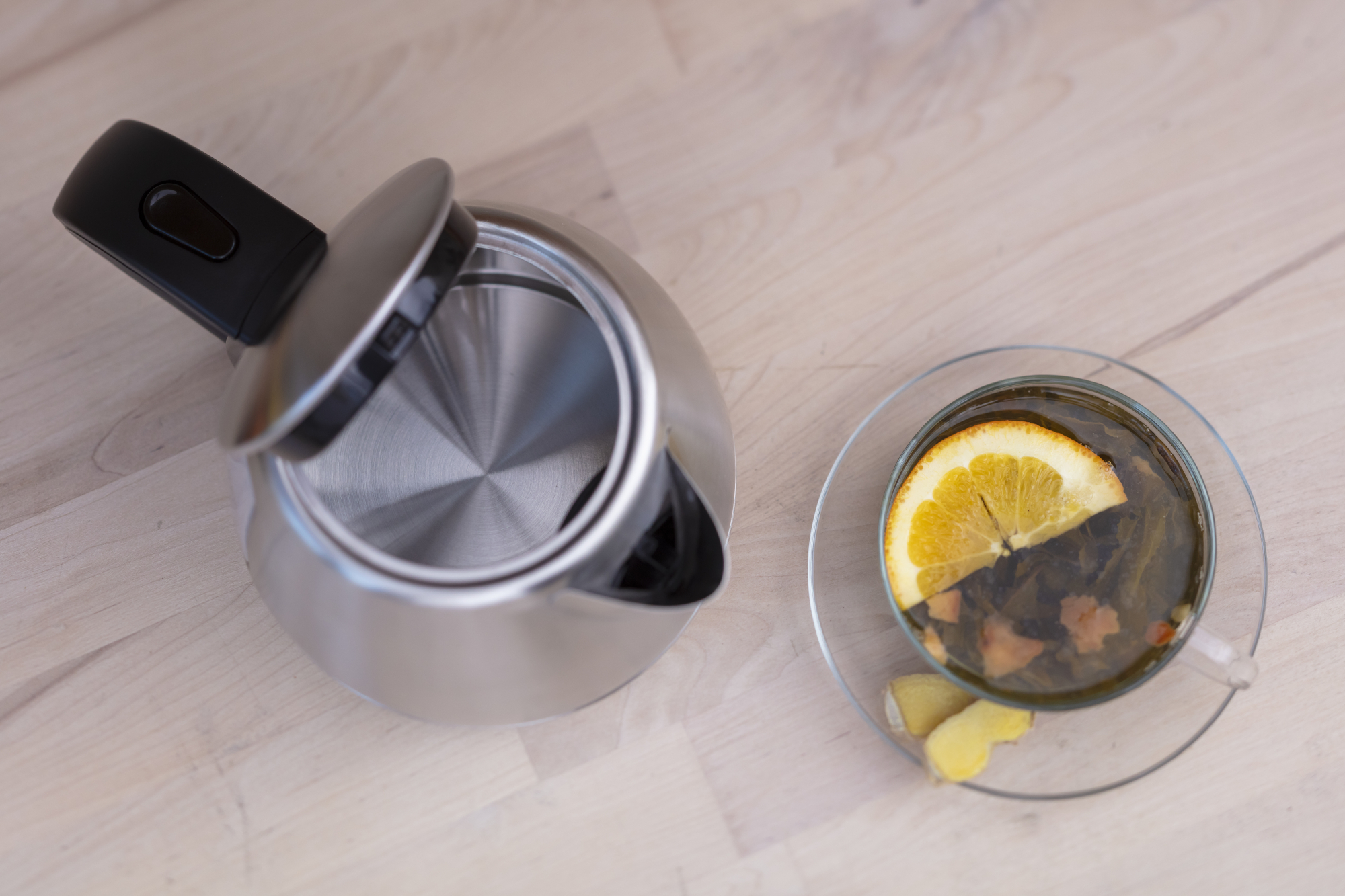 Otwarty czajnik z filiżanką herbaty i plasterkiem cytryny na drewnianym stole.