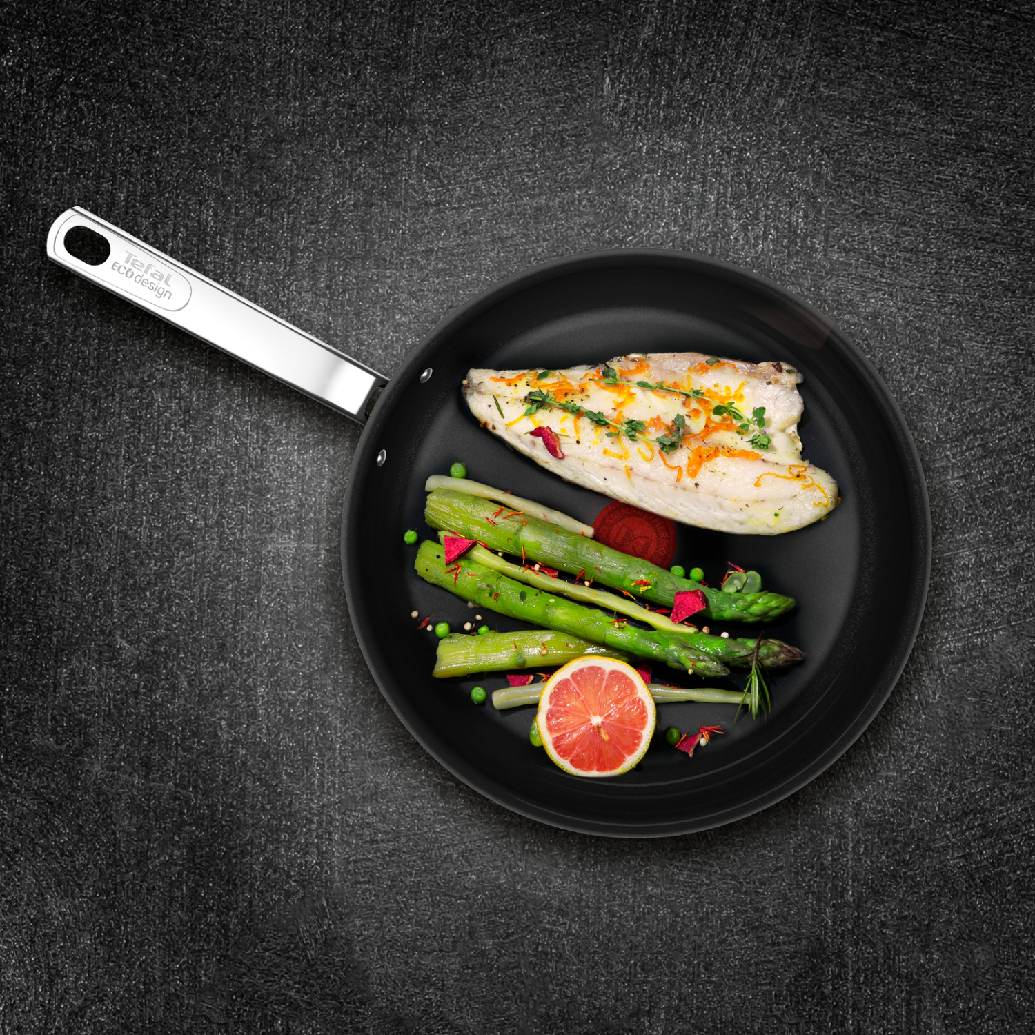 A pan with cooked fish and vegetables, on a dark surface with the tefal logo on the handle.