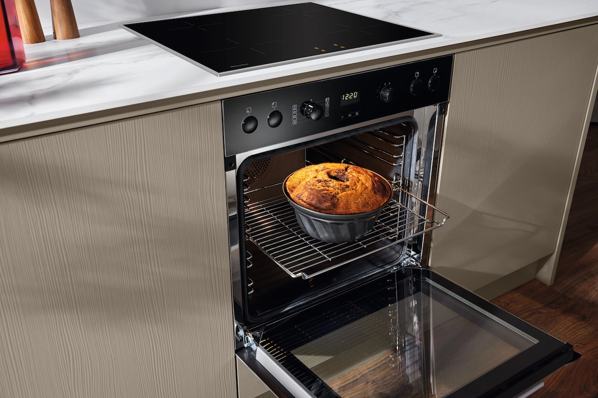 Backofen in einer Küche, mit Kuchen und einem schwarzen Kochfeld darüber.