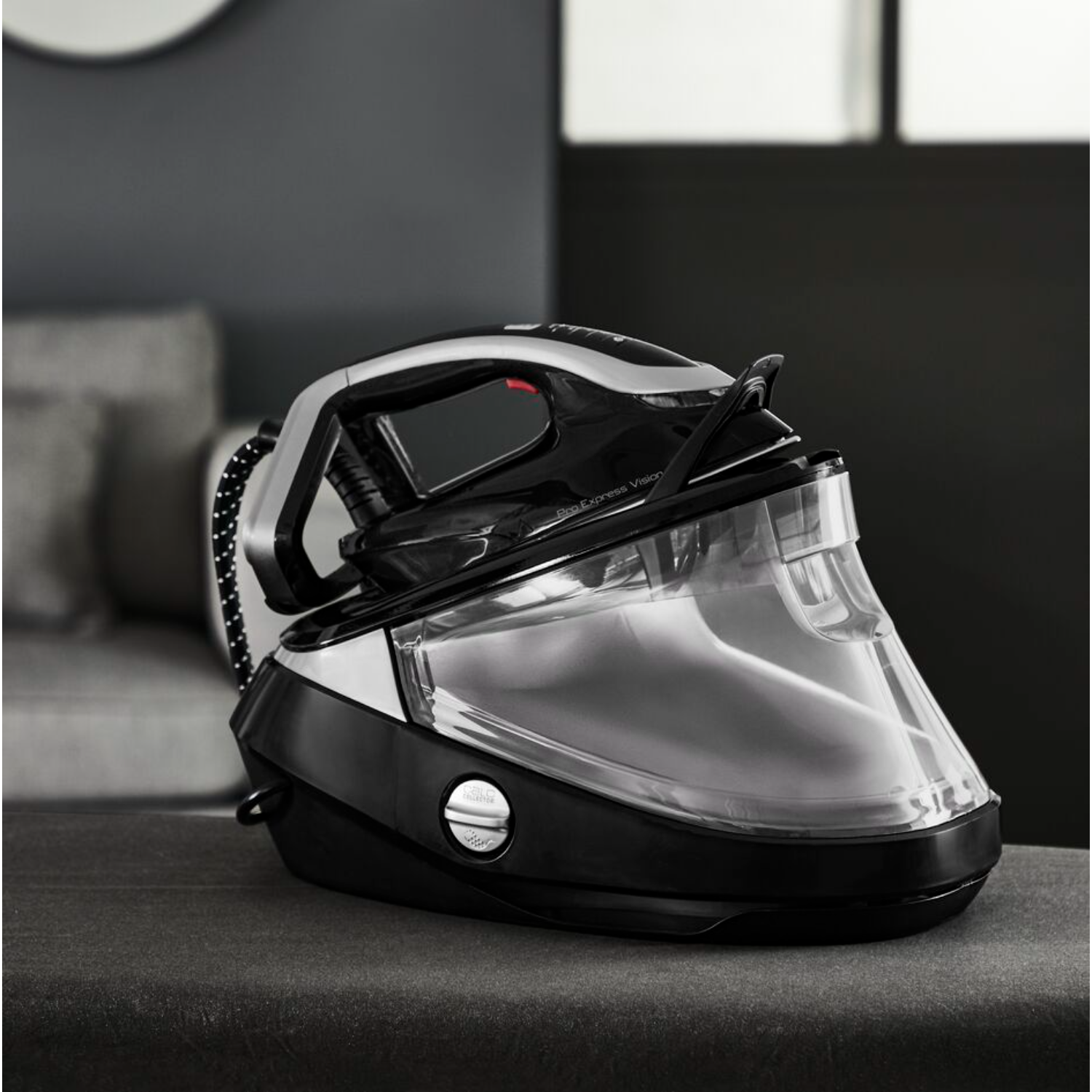 A black and silver iron with a transparent water tank, sitting on a dark gray surface.