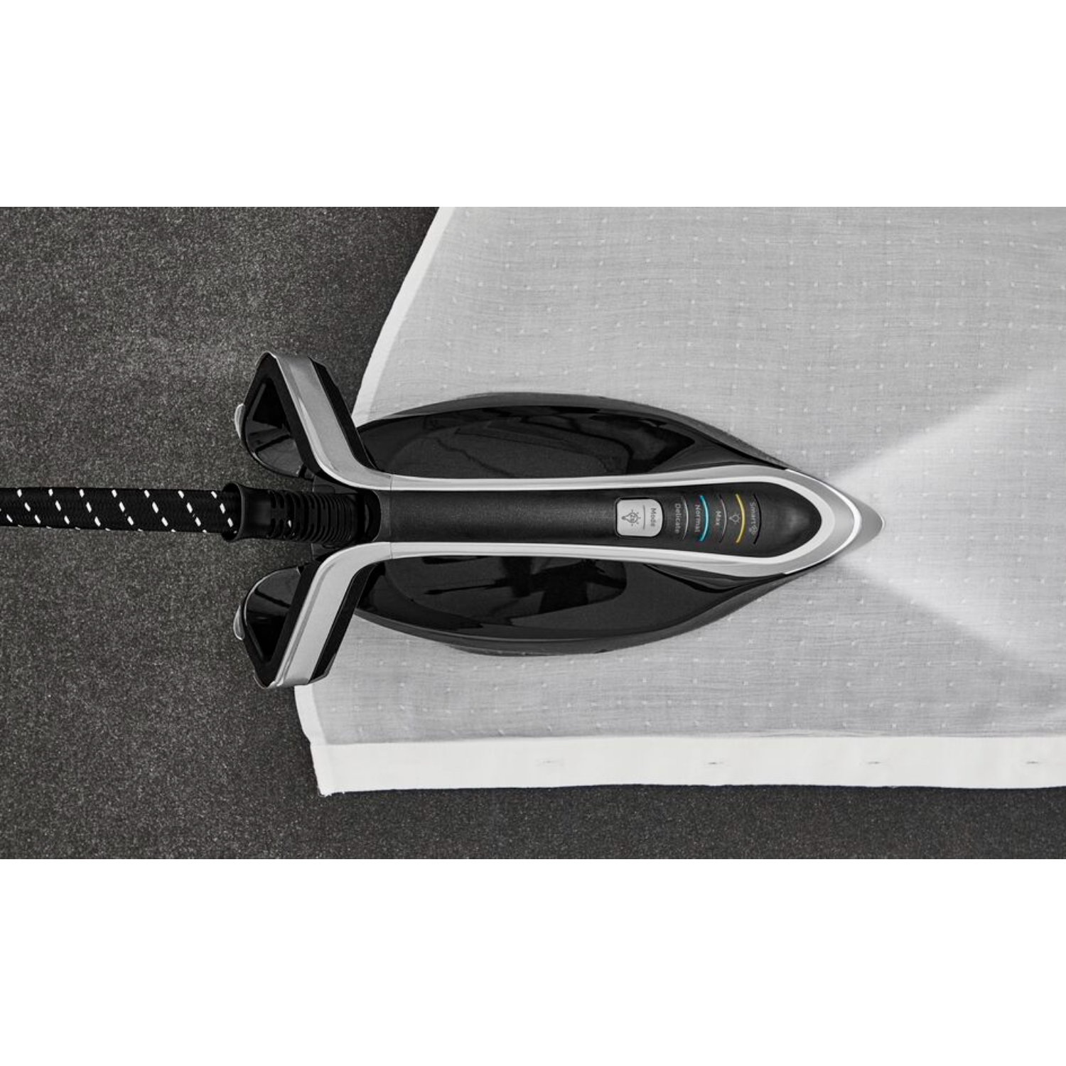 An iron on a board, top view. The iron is black and gray, with a white light shining.