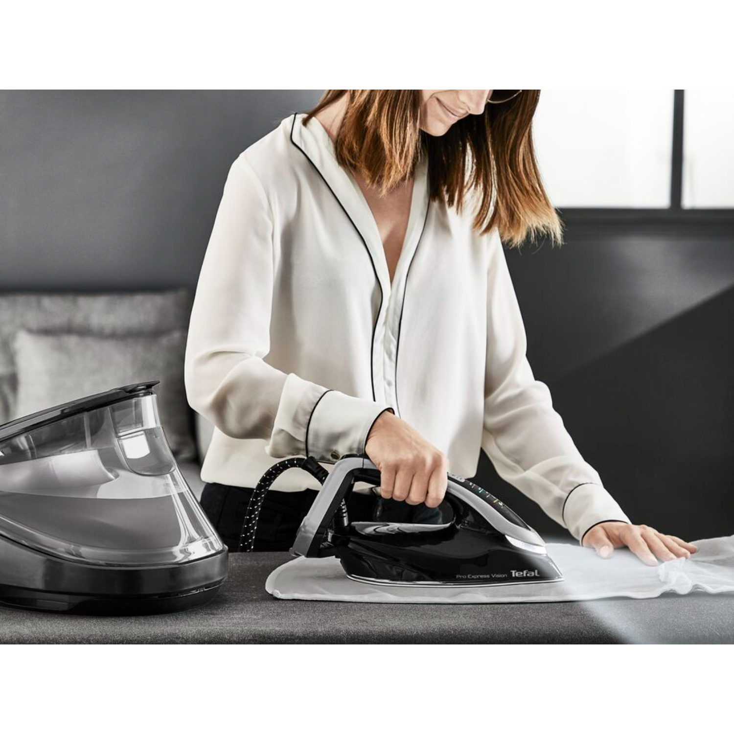 Woman ironing a white shirt with a black iron on a grey ironing board.