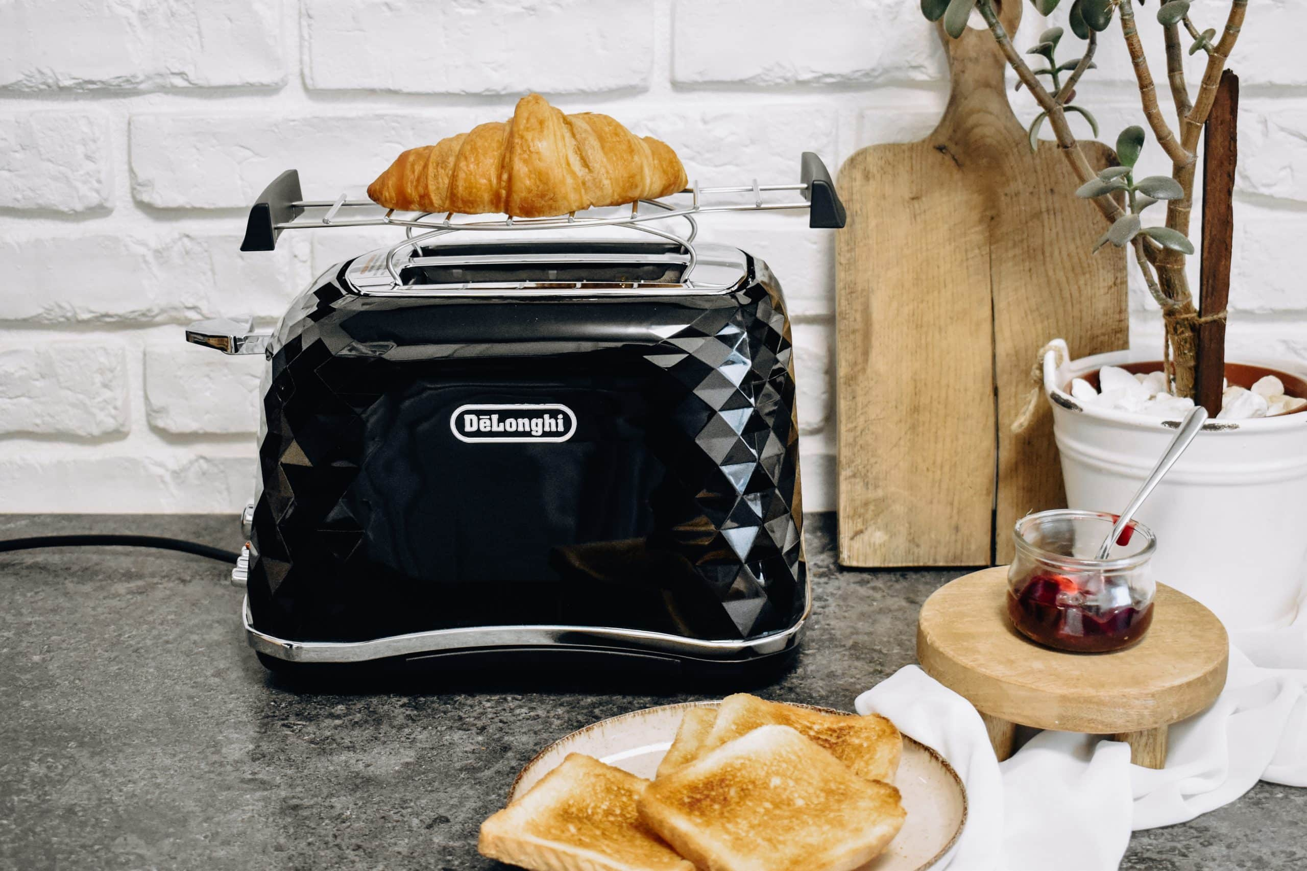 Czarny toster w romby z rogalem na górze i tostem na talerzu.