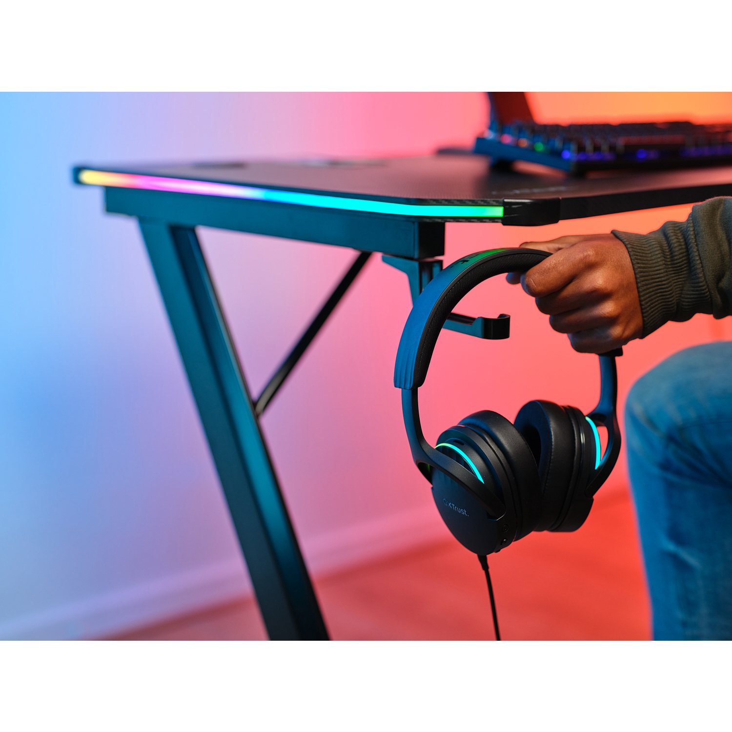 Una persona che tiene un paio di cuffie vicino a una scrivania da gioco nera con luci a LED colorate.