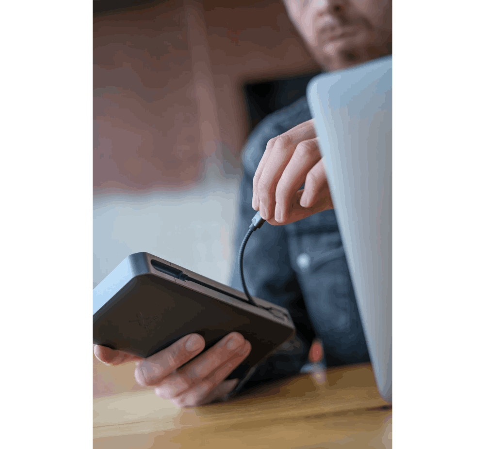 Persona conectando un cable USB-C a un disco duro portátil gris.