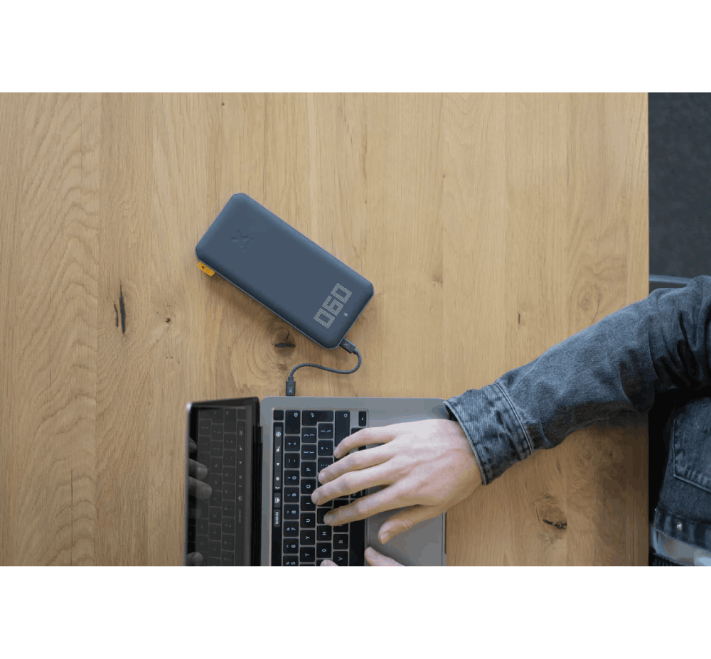 Una persona usando una laptop, con un banco de energía. Mesa de madera.