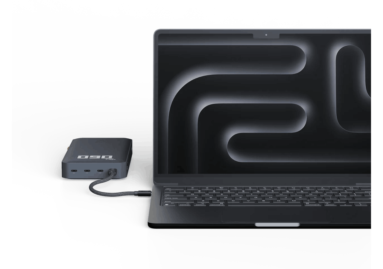 Una laptop negra junto a un banco de energía negro, conectada por un cable.