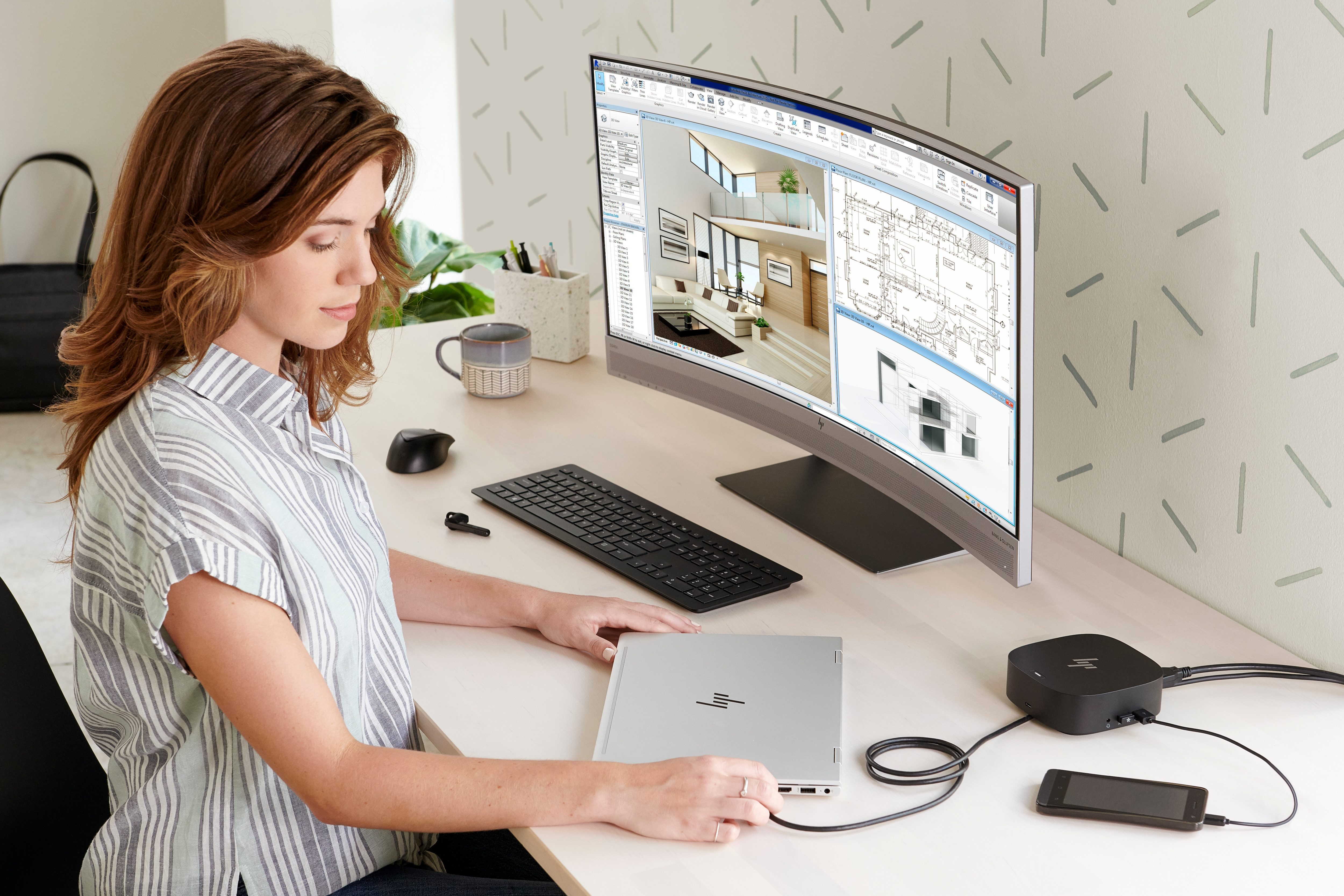 Frau benutzt Laptop an Schreibtisch mit gebogenem Monitor, der Architekturdesign zeigt.