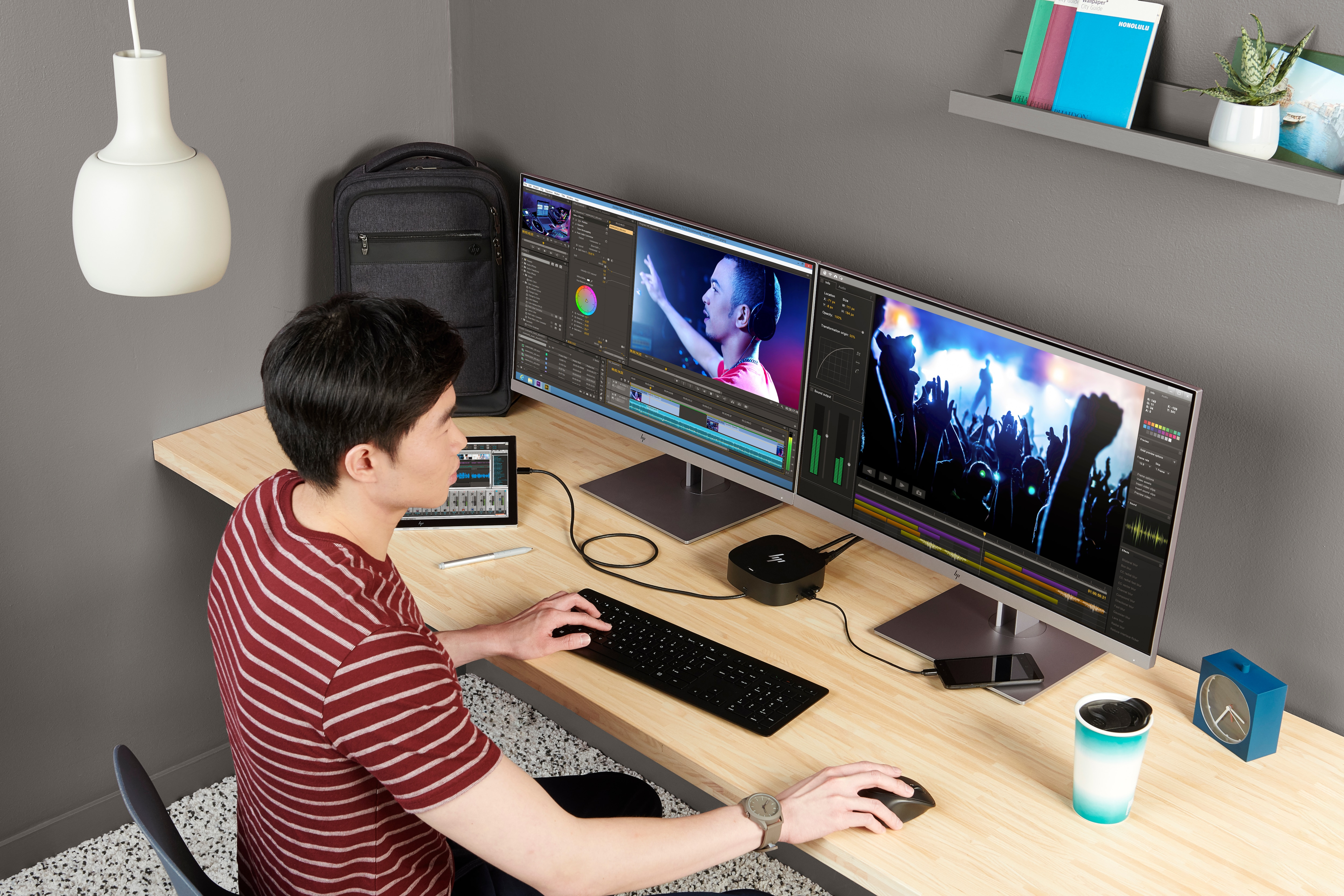 Ein Mann an einem Schreibtisch, der einen Computer mit zwei Monitoren, einer Dockingstation und anderen Gegenständen benutzt.