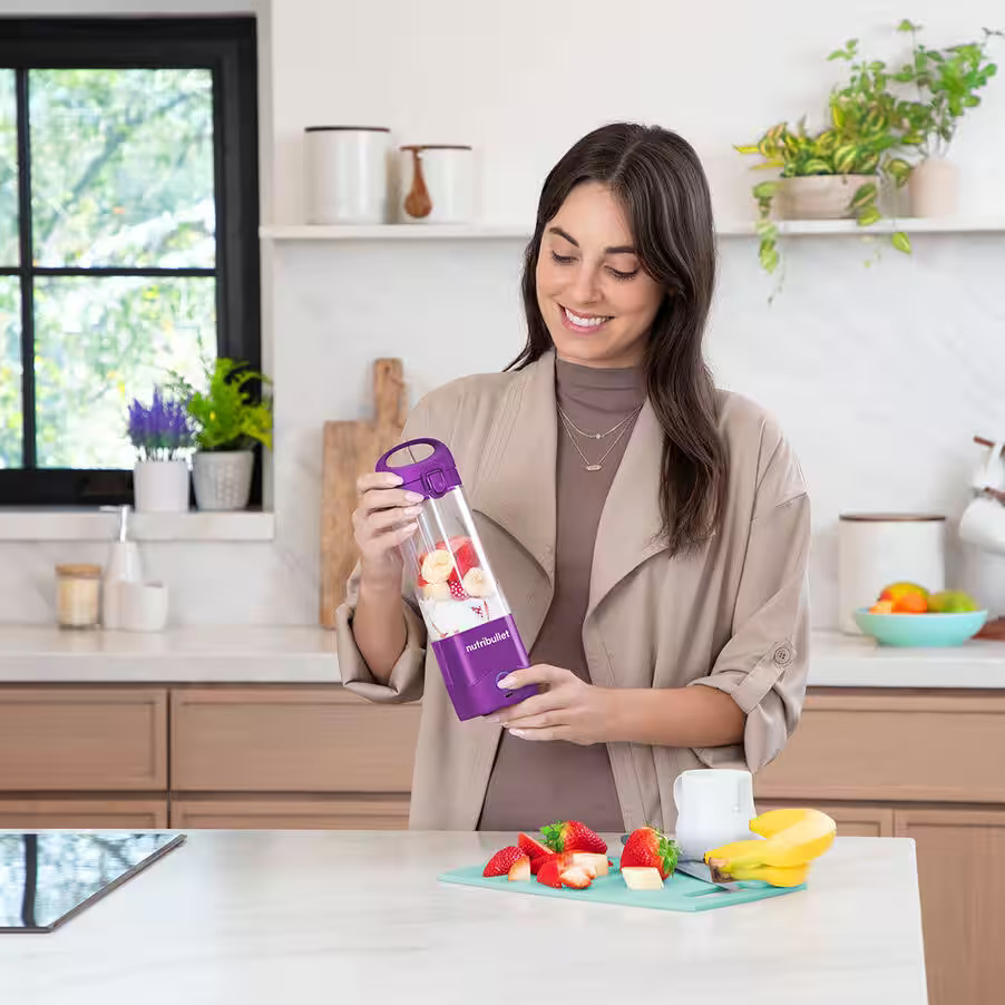 Kobieta trzymająca fioletowy Nutribullet z owocami w kuchni.