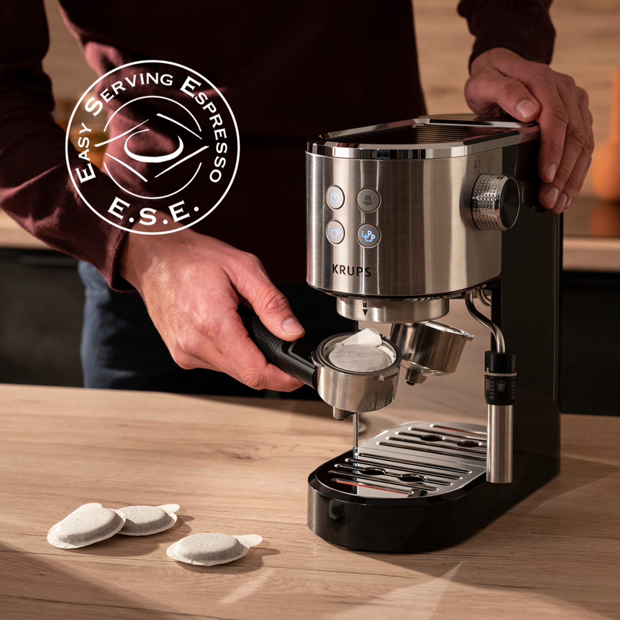 Una persona preparando espresso con una cafetera. Se muestra la etiqueta E.S.E. La marca es Krups.