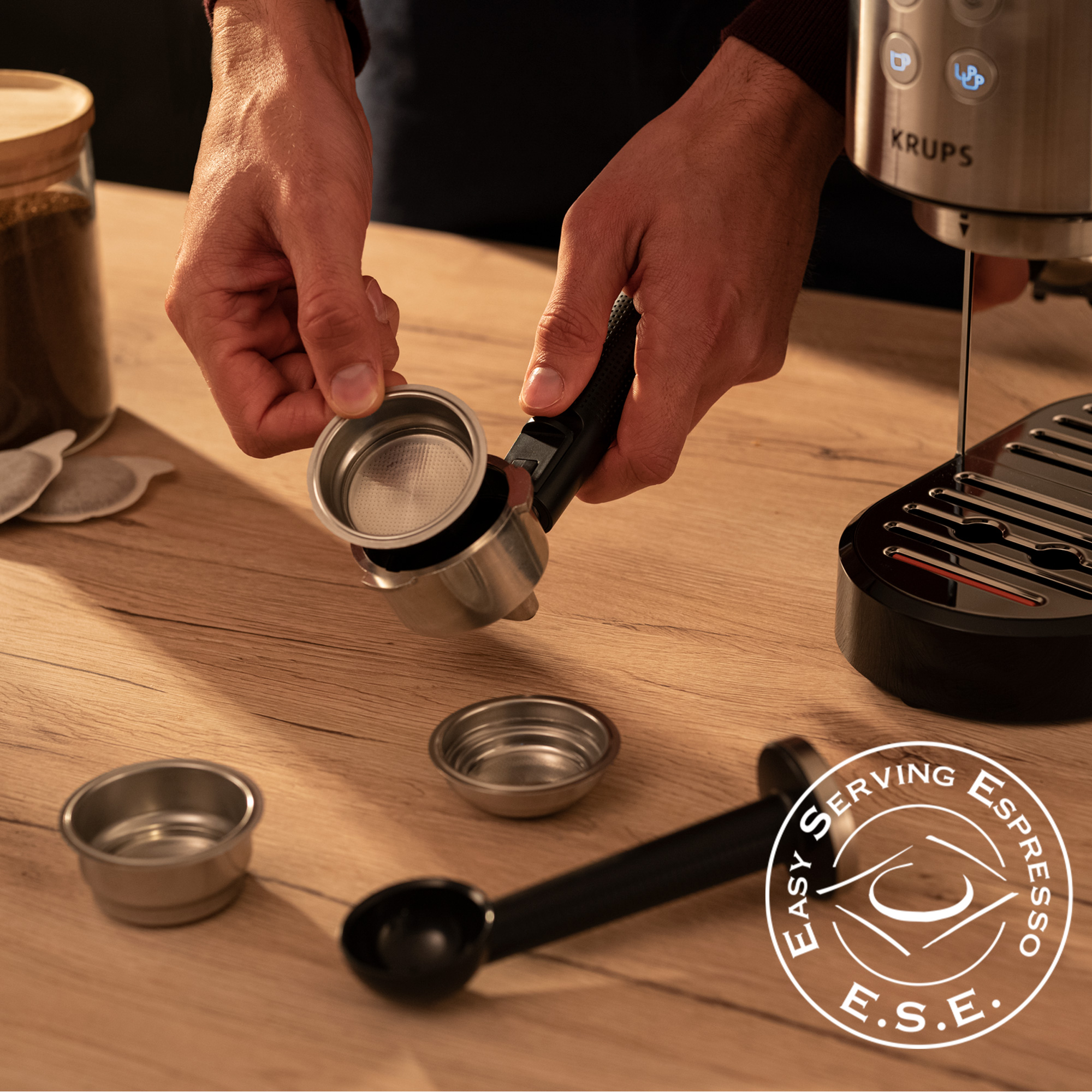 Manos sosteniendo un filtro frente a una máquina de espresso Krups.