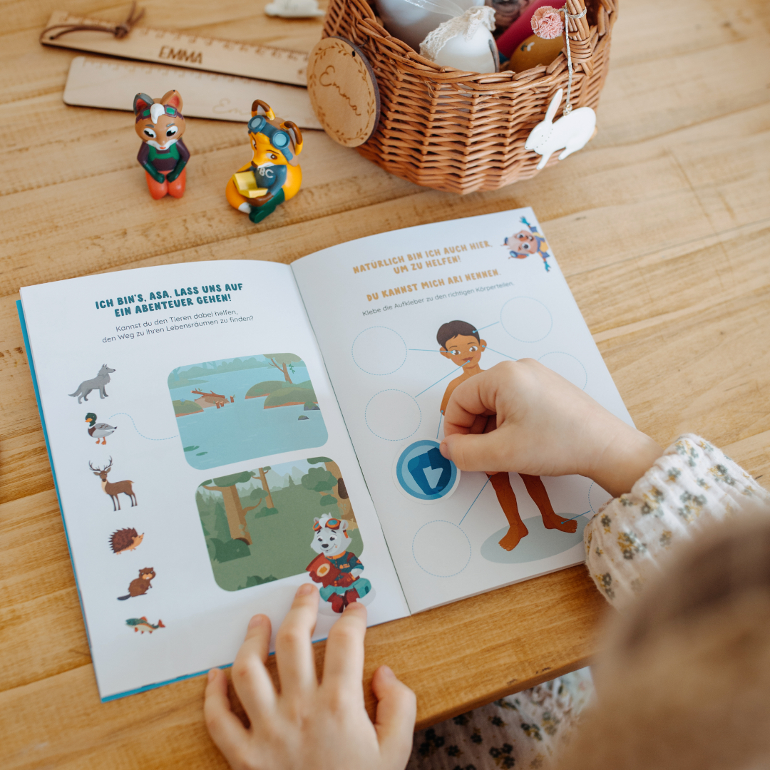Ein Kind interagiert mit einem Buch auf einem Holztisch, Spielzeuge sind in der Nähe.