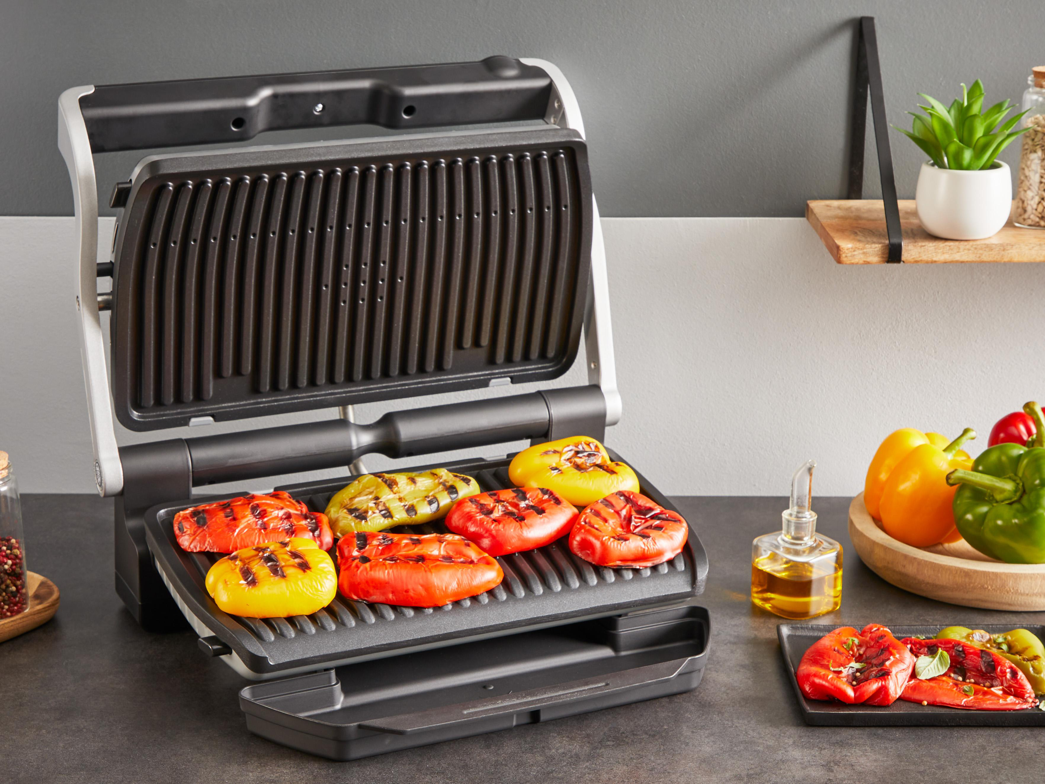 Grill mit gegrillten Paprika. Andere Paprika und Öl im Hintergrund.