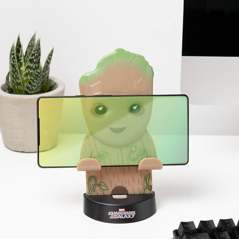 Egy Groot állvány tart egy okostelefont, mellette egy növény és egy billentyűzet.