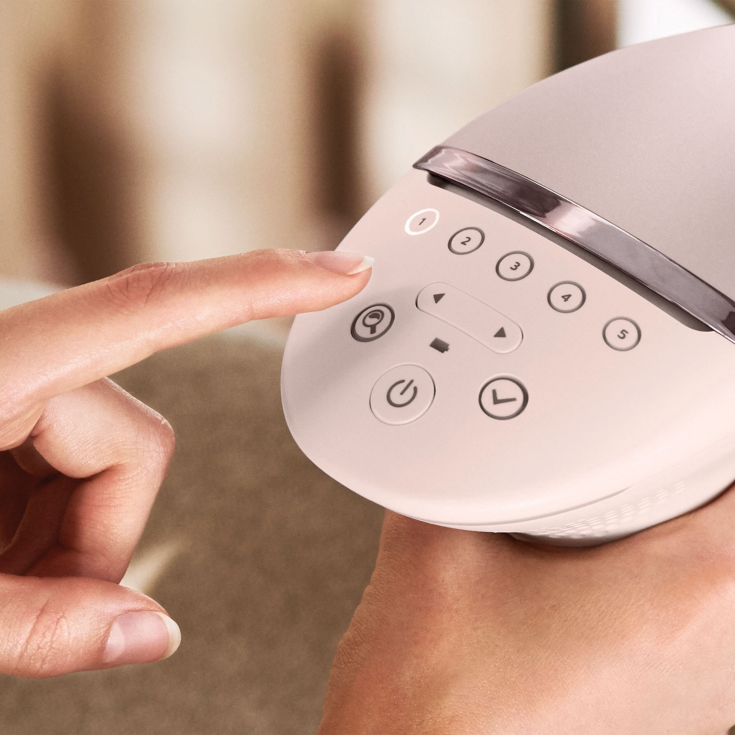 Zbliżenie dłoni naciskającej przyciski na różowym urządzeniu. Przyciski są ponumerowane i opisane.