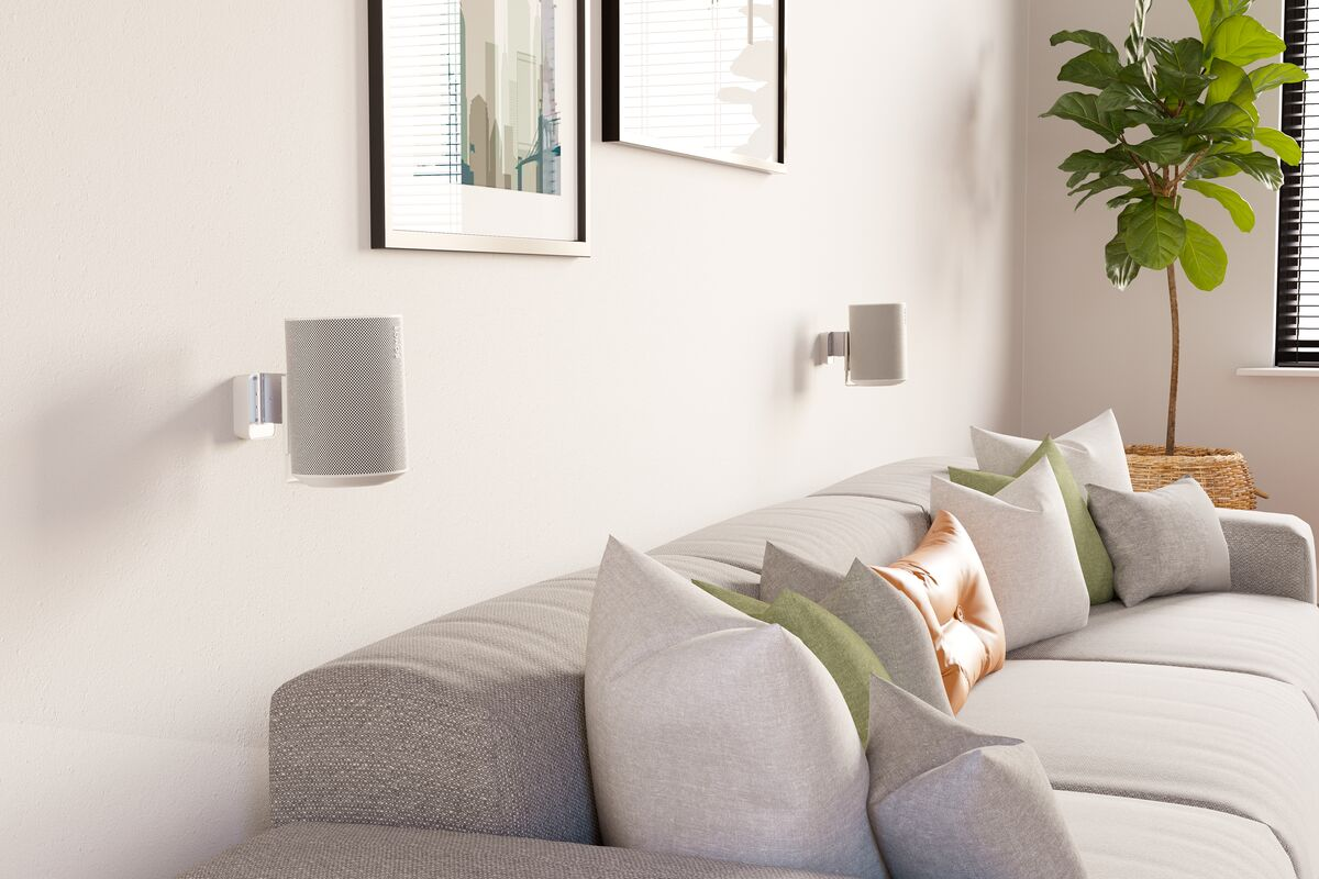 Salón con altavoces montados en la pared sobre un sofá gris, con obras de arte y plantas.