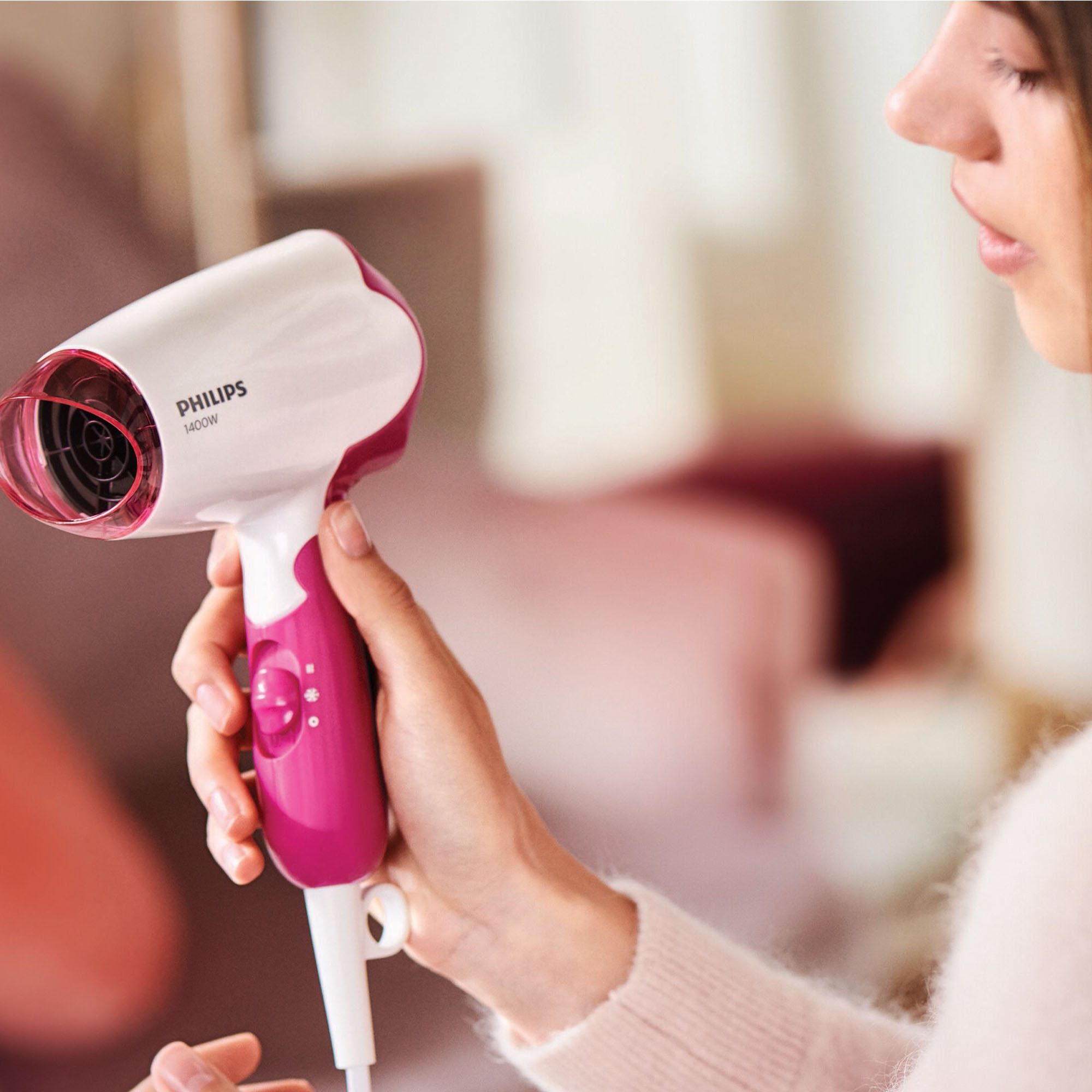 Kobieta trzyma różowo-białą suszarkę do włosów Philips. Marka jest widoczna z boku.