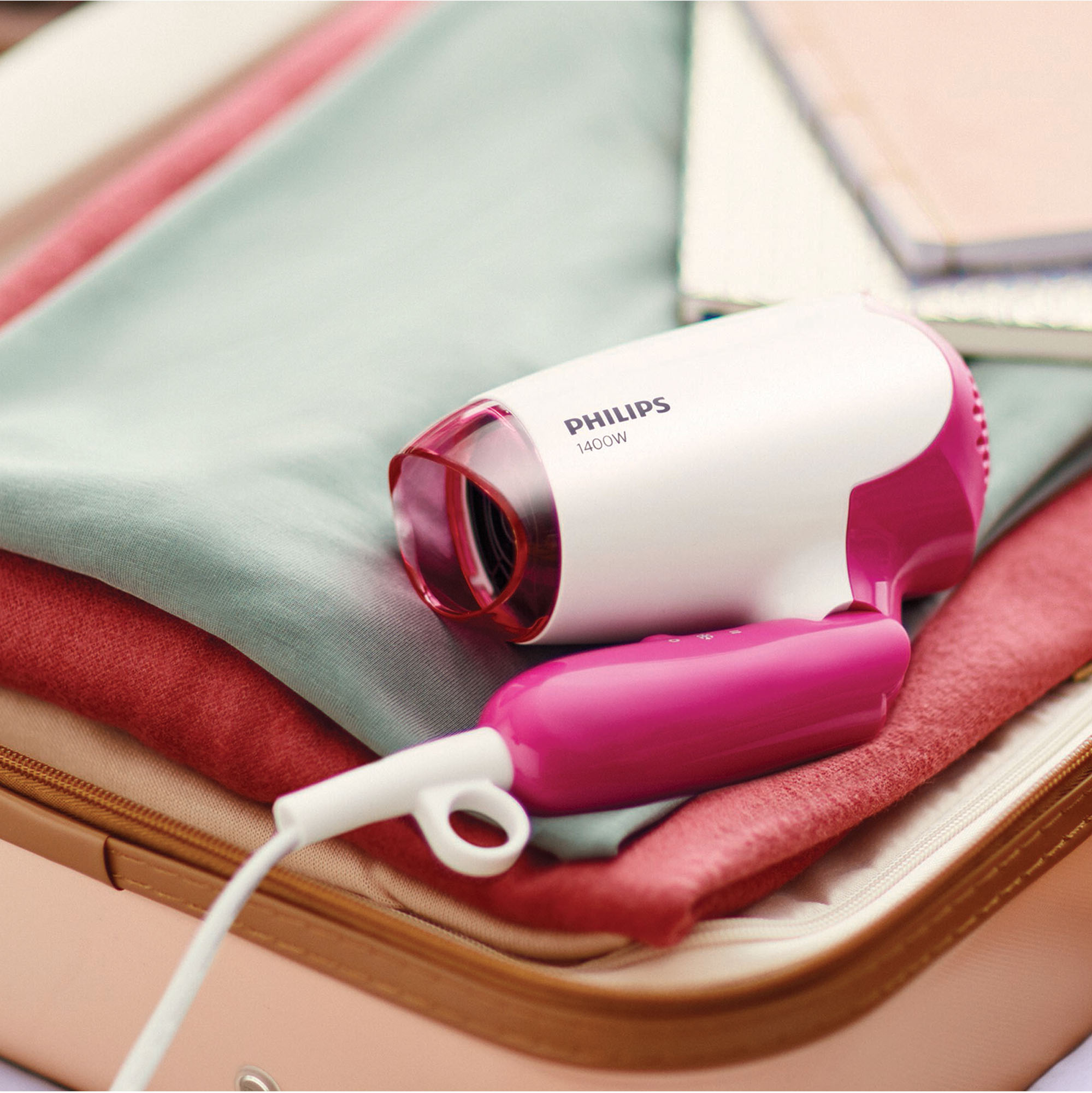 Biała i różowa suszarka do włosów Philips na złożonych ubraniach w walizce.