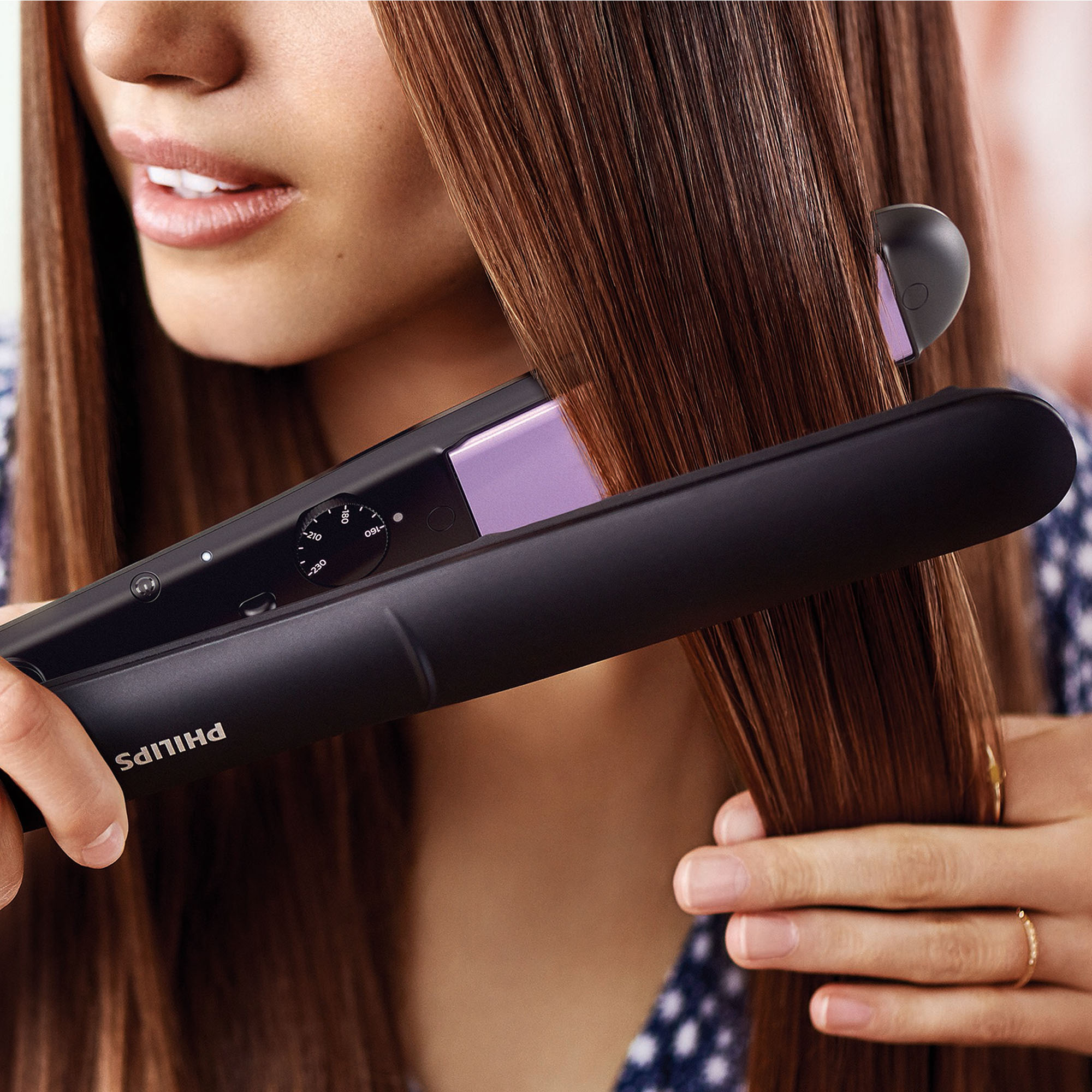 Kobieta prostuje włosy. Używa czarno-fioletowej prostownicy.