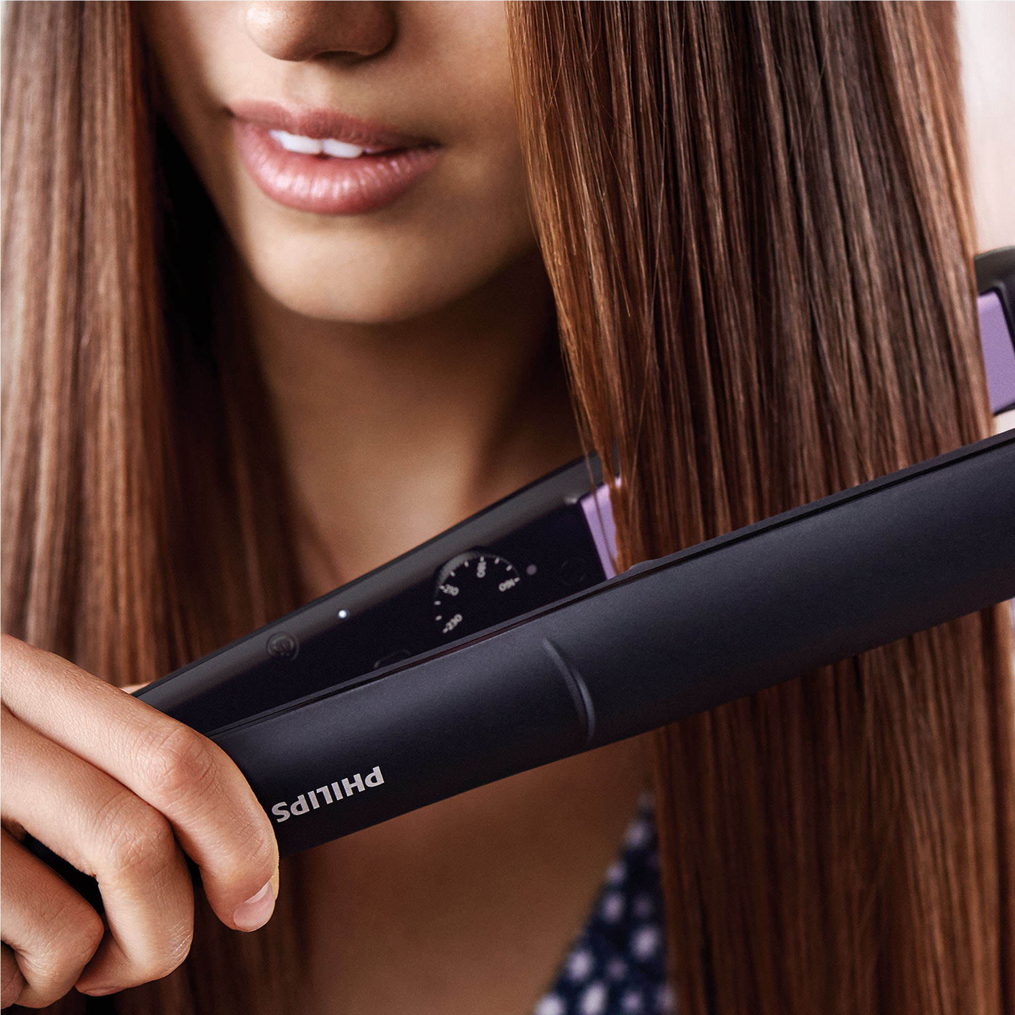 Kobieta używająca czarnej prostownicy do brązowych włosów. Widoczna marka Philips.