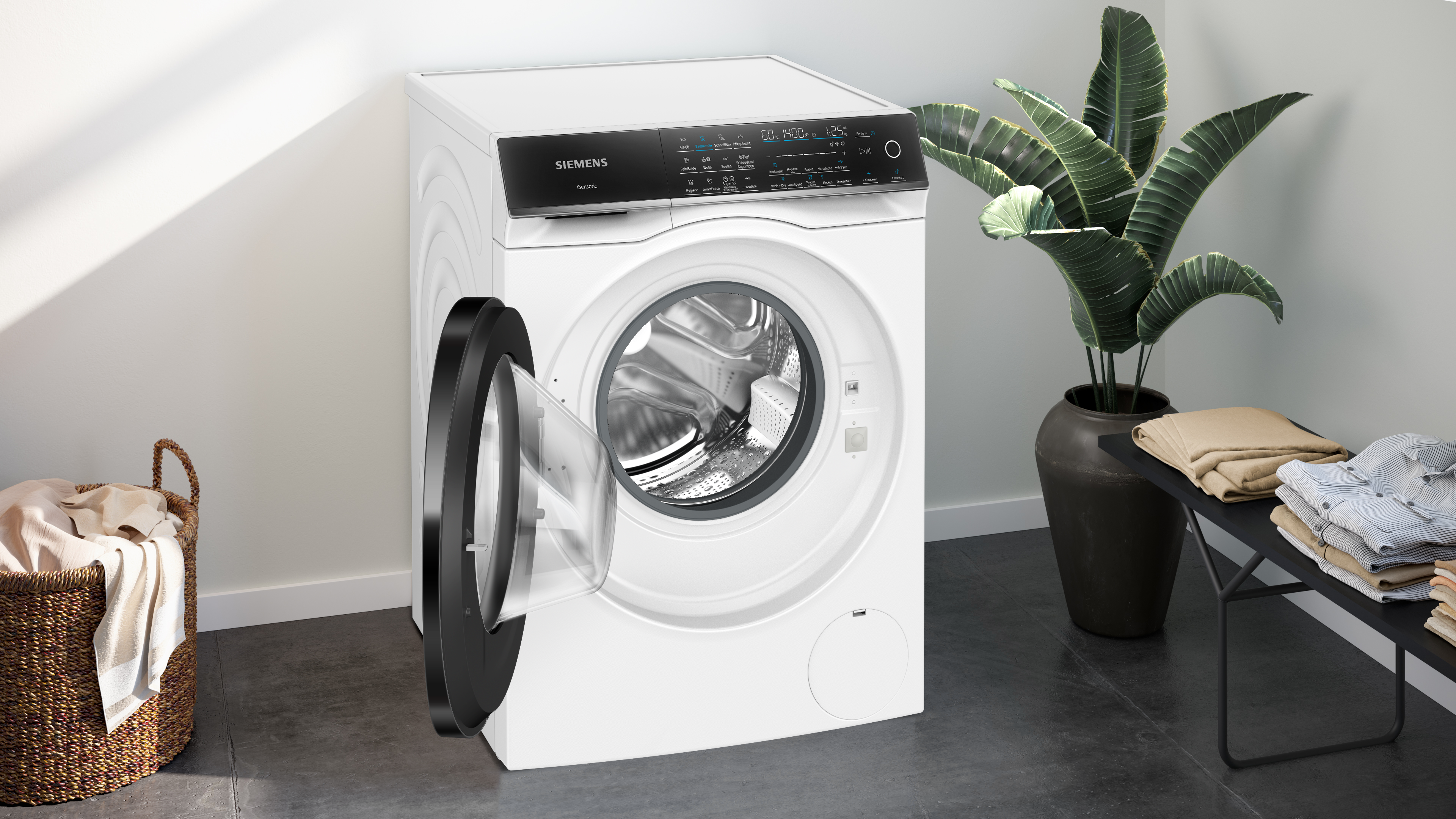 Weiße Waschmaschine mit offener Tür, neben Wäschekorb und Pflanze.