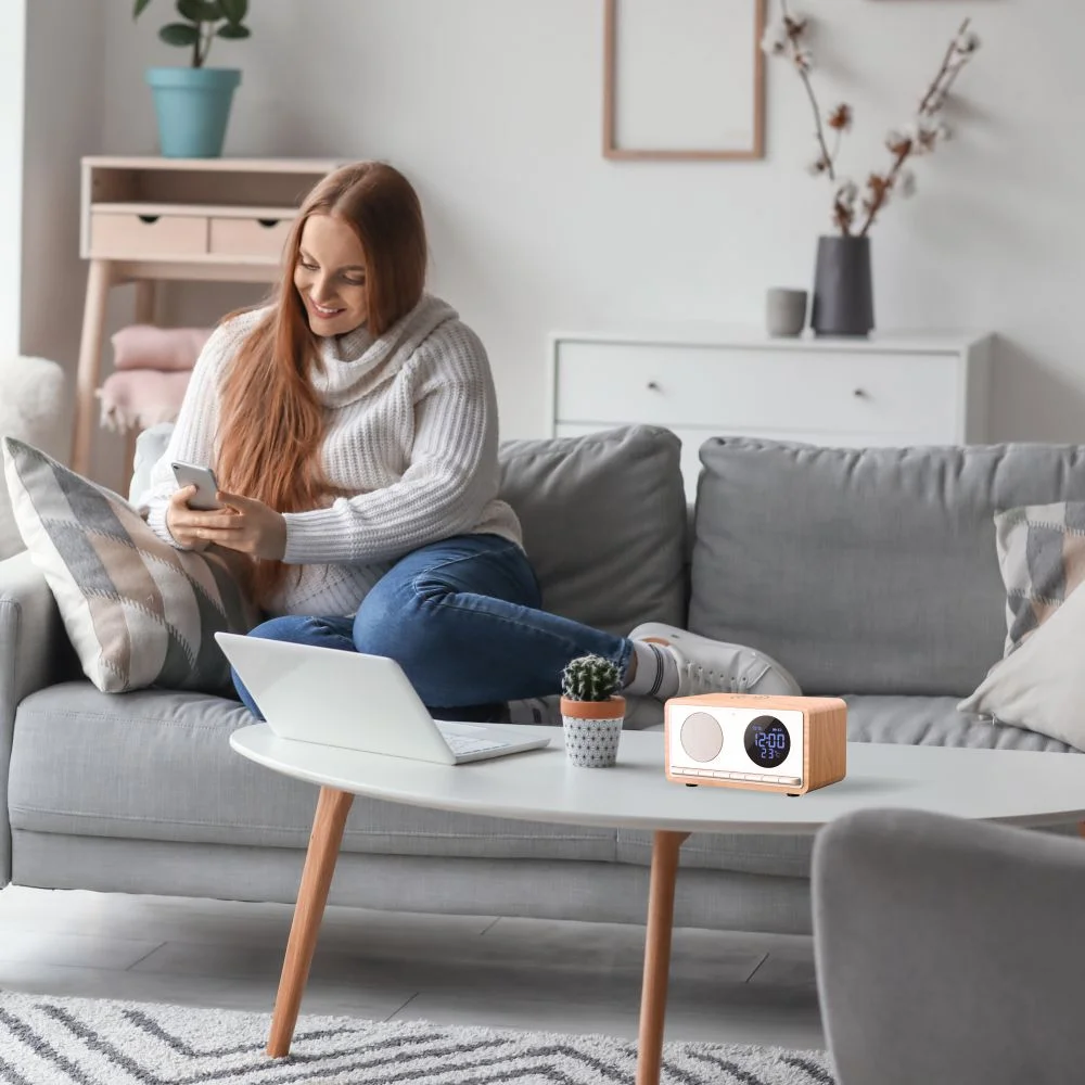 Kobieta siedzi na kanapie, korzystając z telefonu. Laptop i radio na stole. Ustawienia salonu.