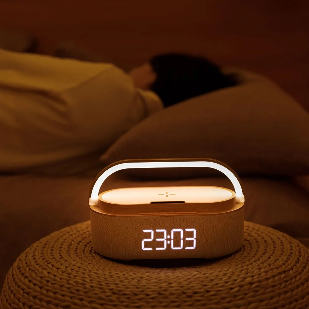 Lampa nocna z zegarem cyfrowym. Wyświetla godzinę 23:03. Osoba śpiąca w tle.