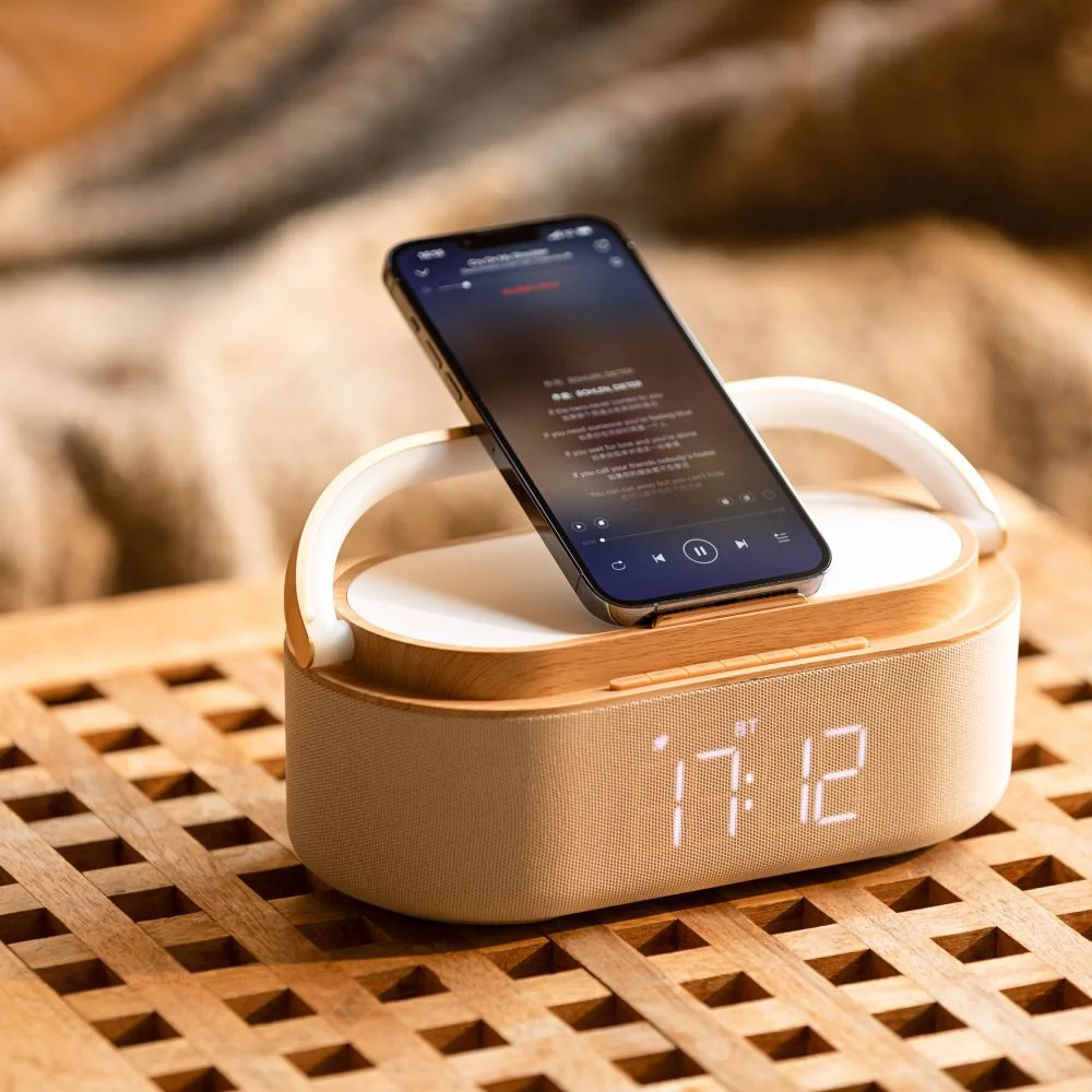 Drewniany głośnik z telefonem na górze, wyświetlającym aplikację muzyczną. Godzina 17:12 na głośniku.