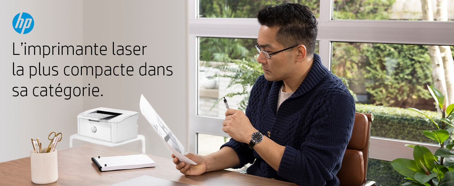 Mann mit Brille betrachtet Papier, hält Stift. Drucker, Schreibtisch und Fenster im Hintergrund. HP-Logo sichtbar.