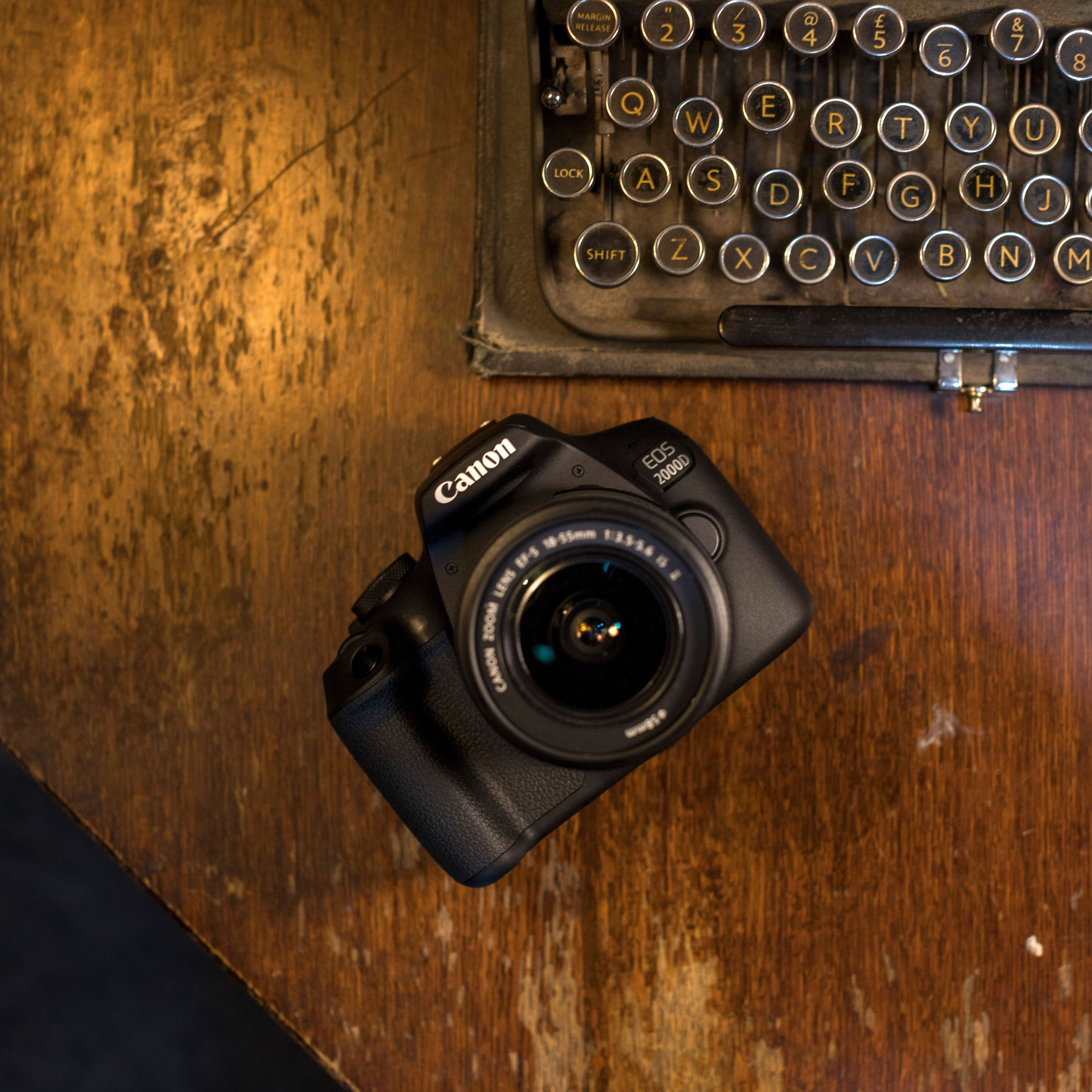 Una fotocamera Canon EOS 2000D è su un tavolo di legno, con una macchina da scrivere d'epoca sullo sfondo.