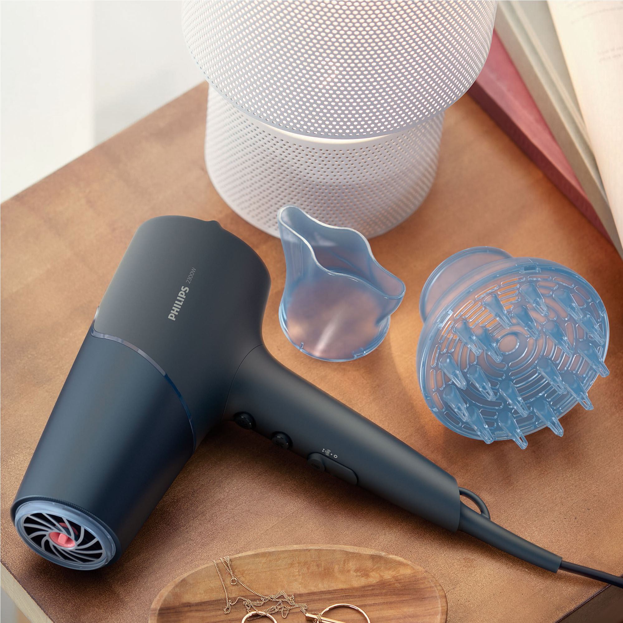 Suszarka do włosów i akcesoria na stole. Suszarka jest czarna, z niebieskimi nakładkami. Drewniana powierzchnia.