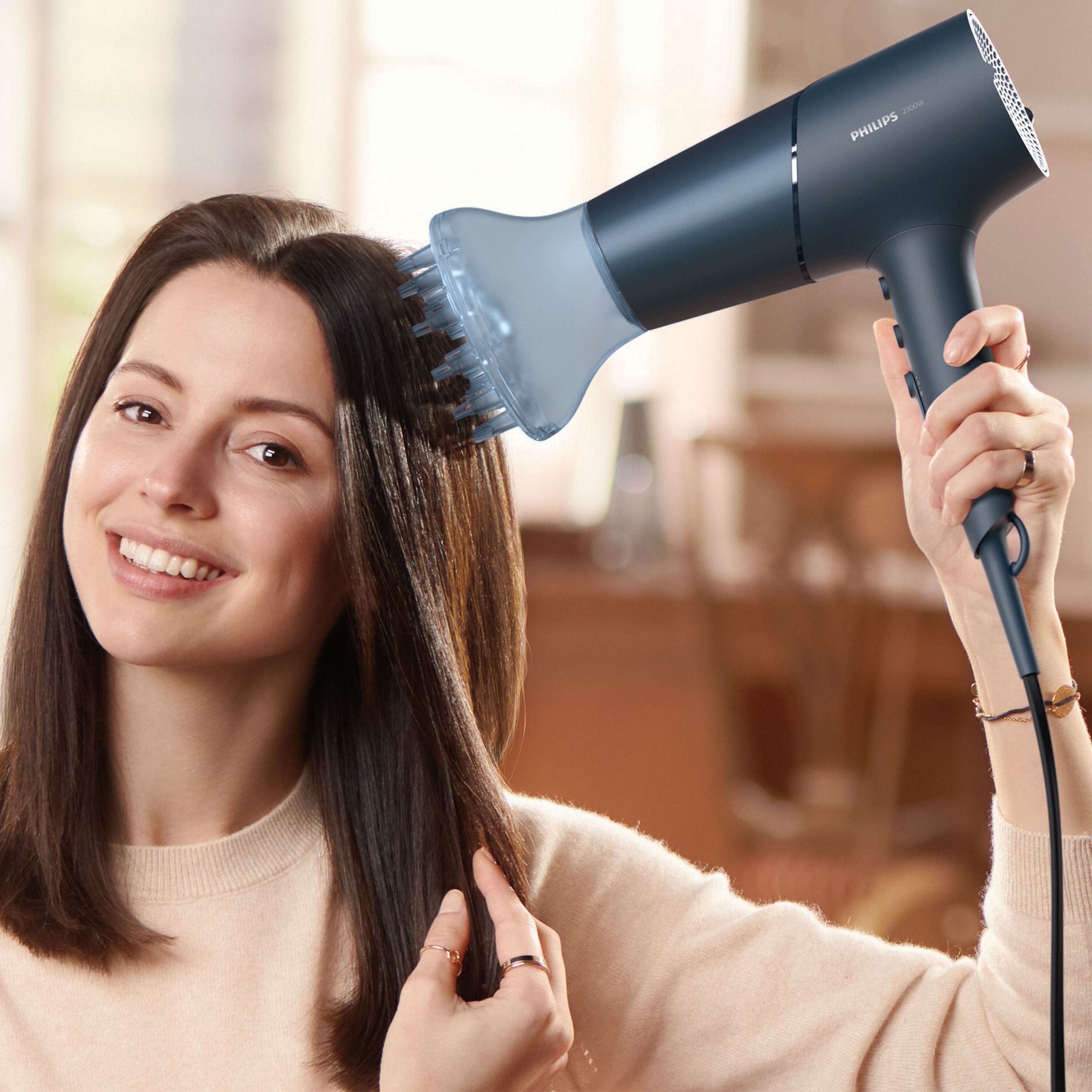 Kobieta używa suszarki do włosów. Uśmiecha się. Suszarka jest granatowa z dyfuzorem.