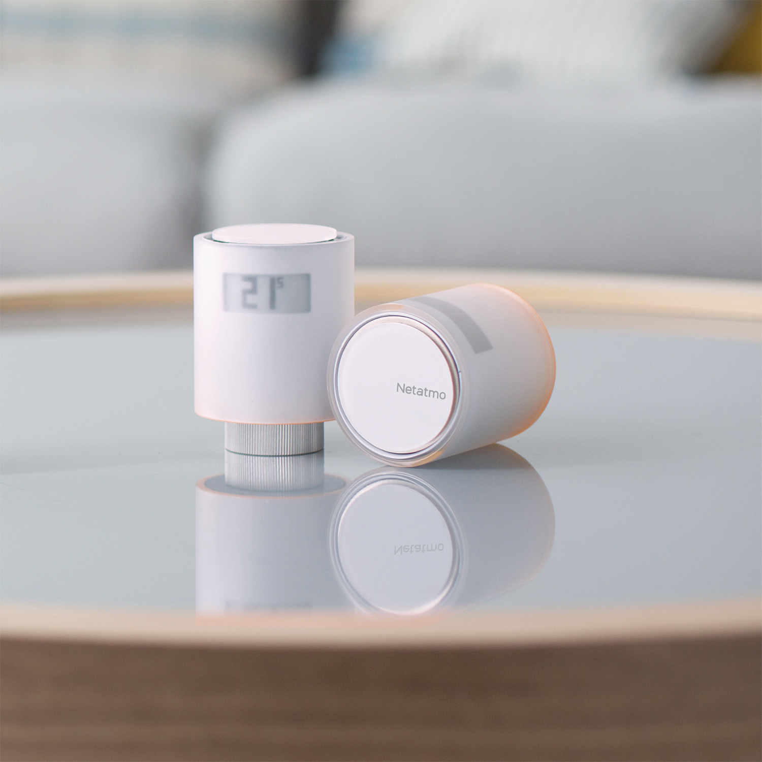 Due termostati intelligenti Netatmo bianchi su vetro. Uno mostra '21'. Riflesso visibile.