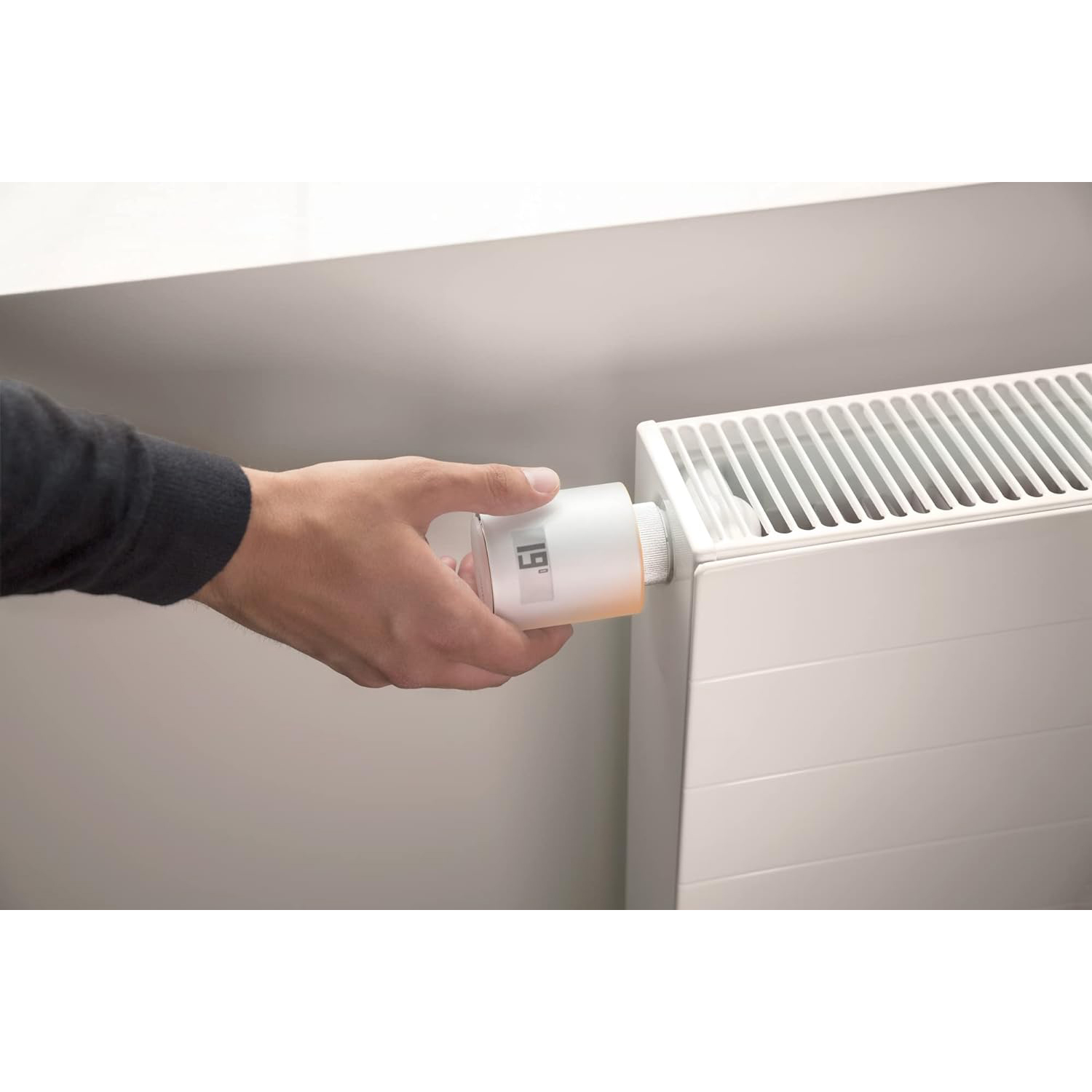 Una mano che regola un termostato bianco su un radiatore bianco. Il display mostra il numero 19.