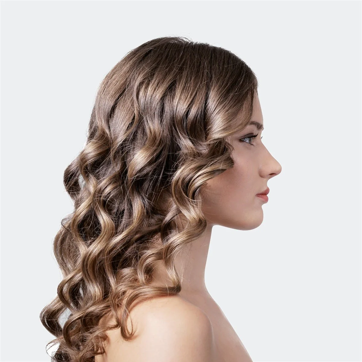 Une femme aux cheveux bruns ondulés, regardant vers la droite, est montrée de profil sur fond blanc.