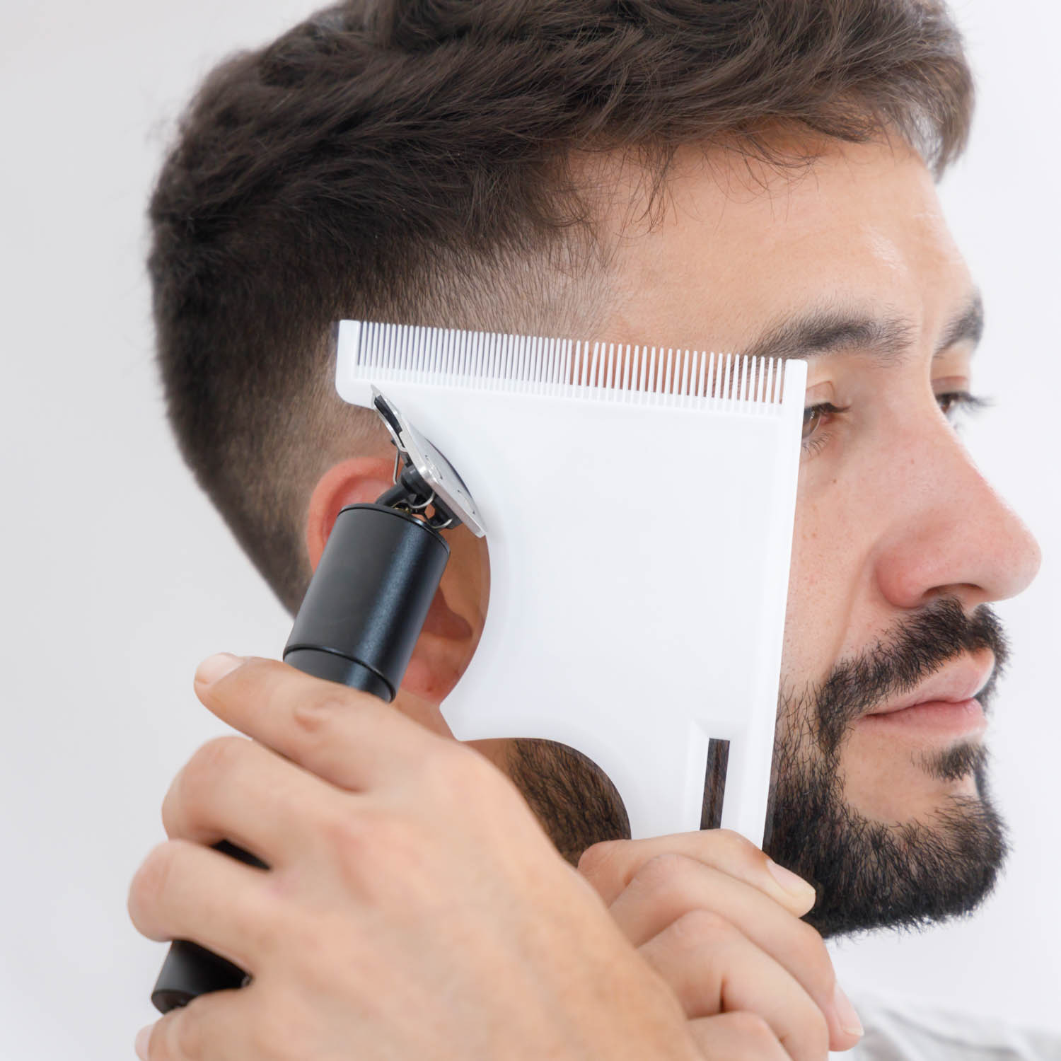 Un hombre usando una recortadora de cabello con una guía de peine para recortar su barba.