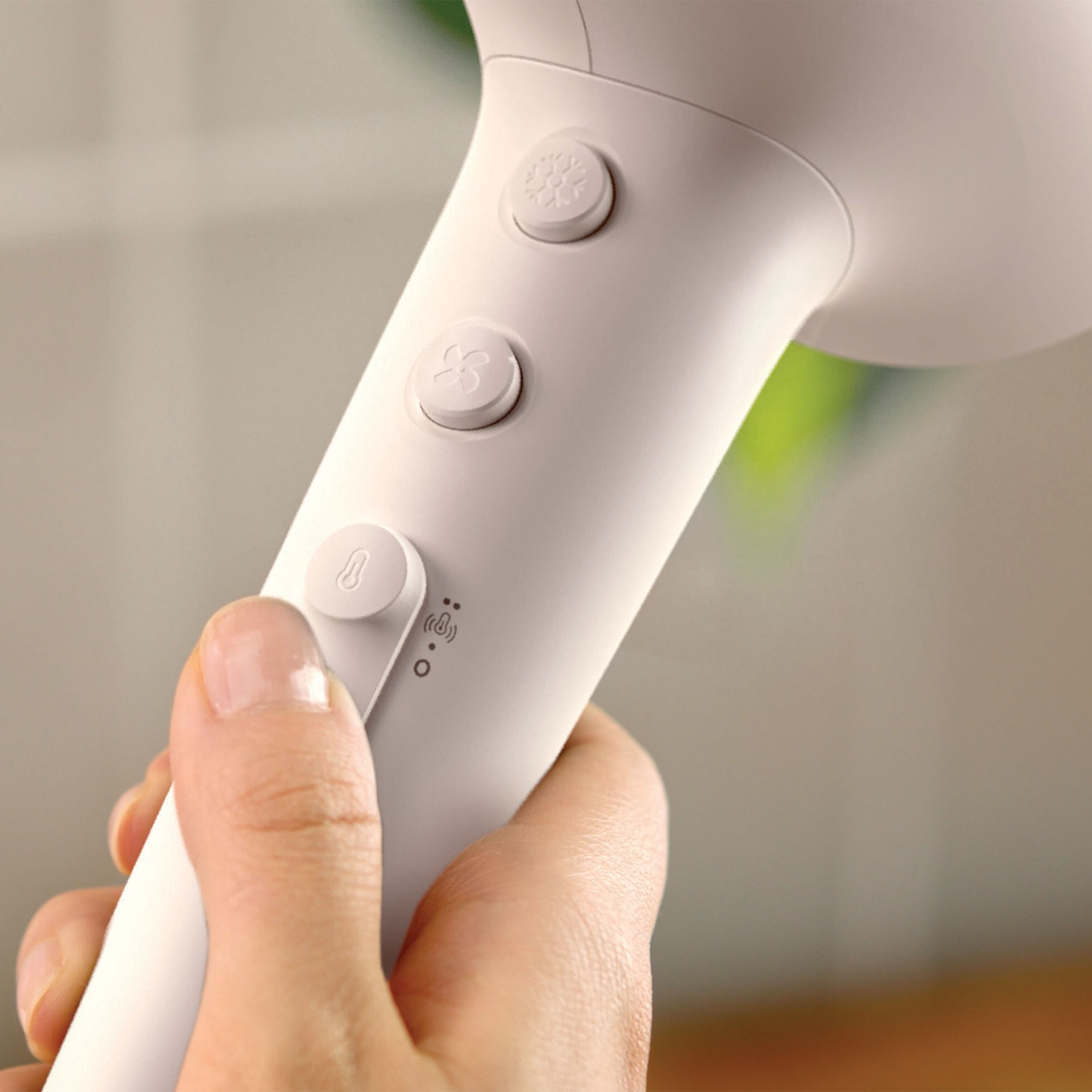 Dłoń trzymająca białą suszarkę do włosów z przyciskami sterowania, zbliżenie.