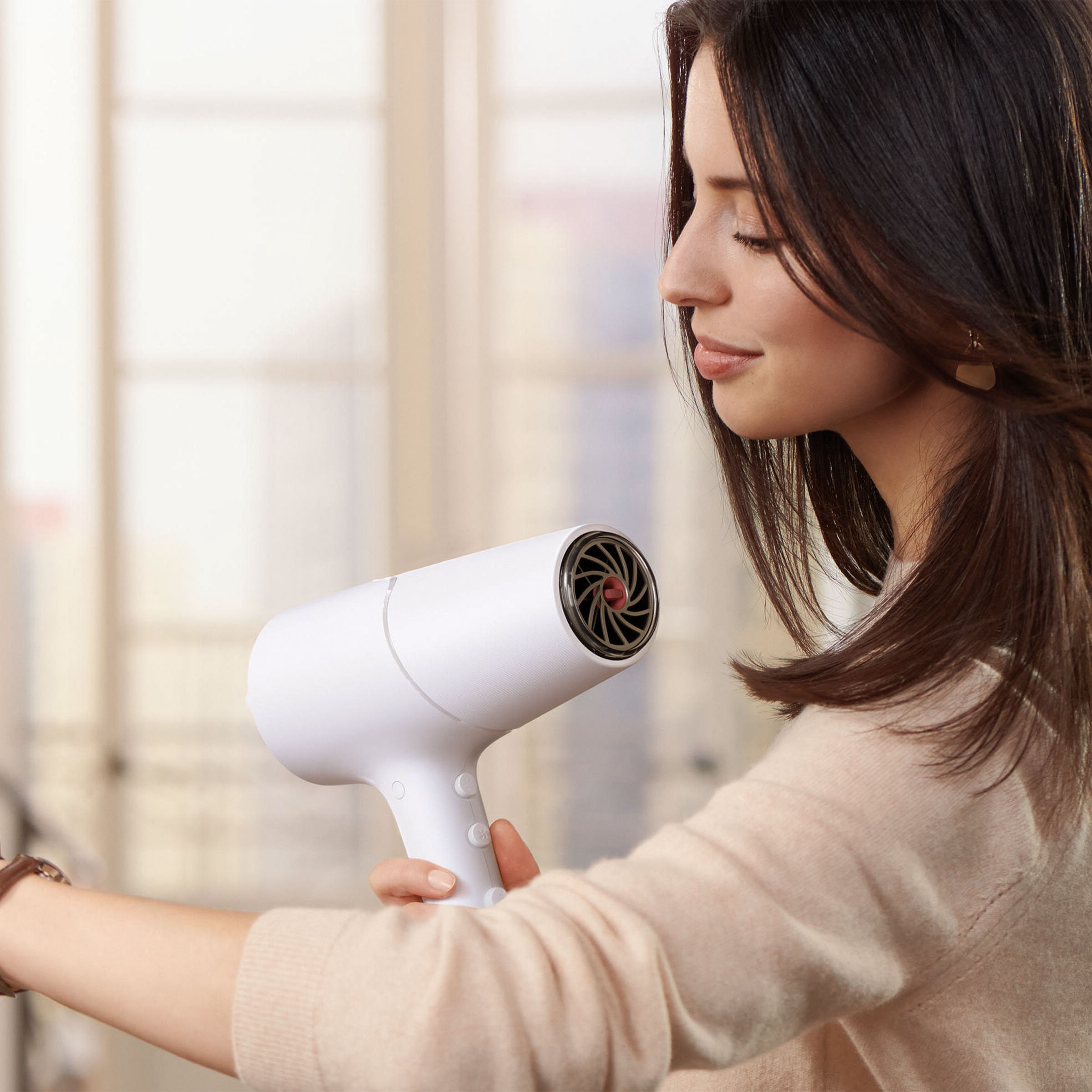 Kobieta trzymająca białą suszarkę do włosów. Kobieta trzyma suszarkę do włosów. Kobieta z brązowymi włosami. Tło rozmyte.