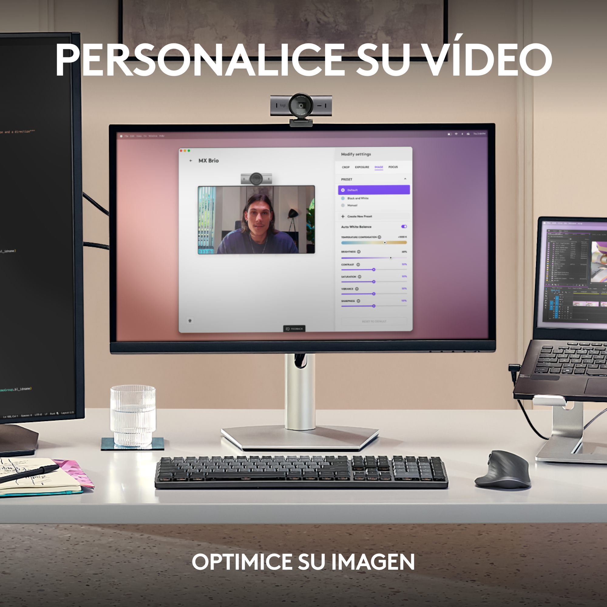 Un espacio de trabajo con un monitor mostrando un video, un teclado, un ratón, un vaso y un portátil.