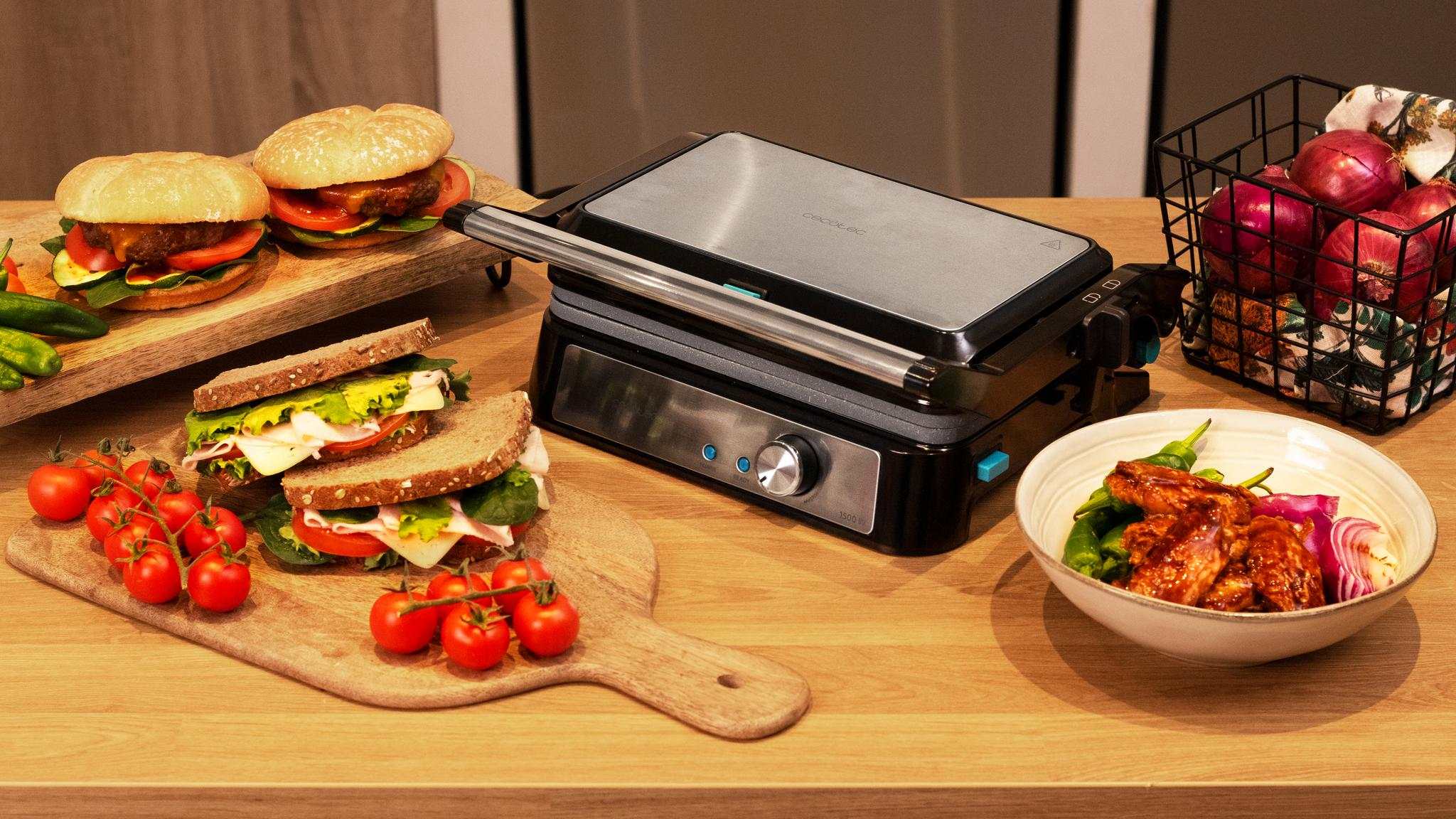 Sándwiches, hamburguesas y una parrilla sobre una mesa de madera. También hay verduras y un cuenco con comida cocinada.