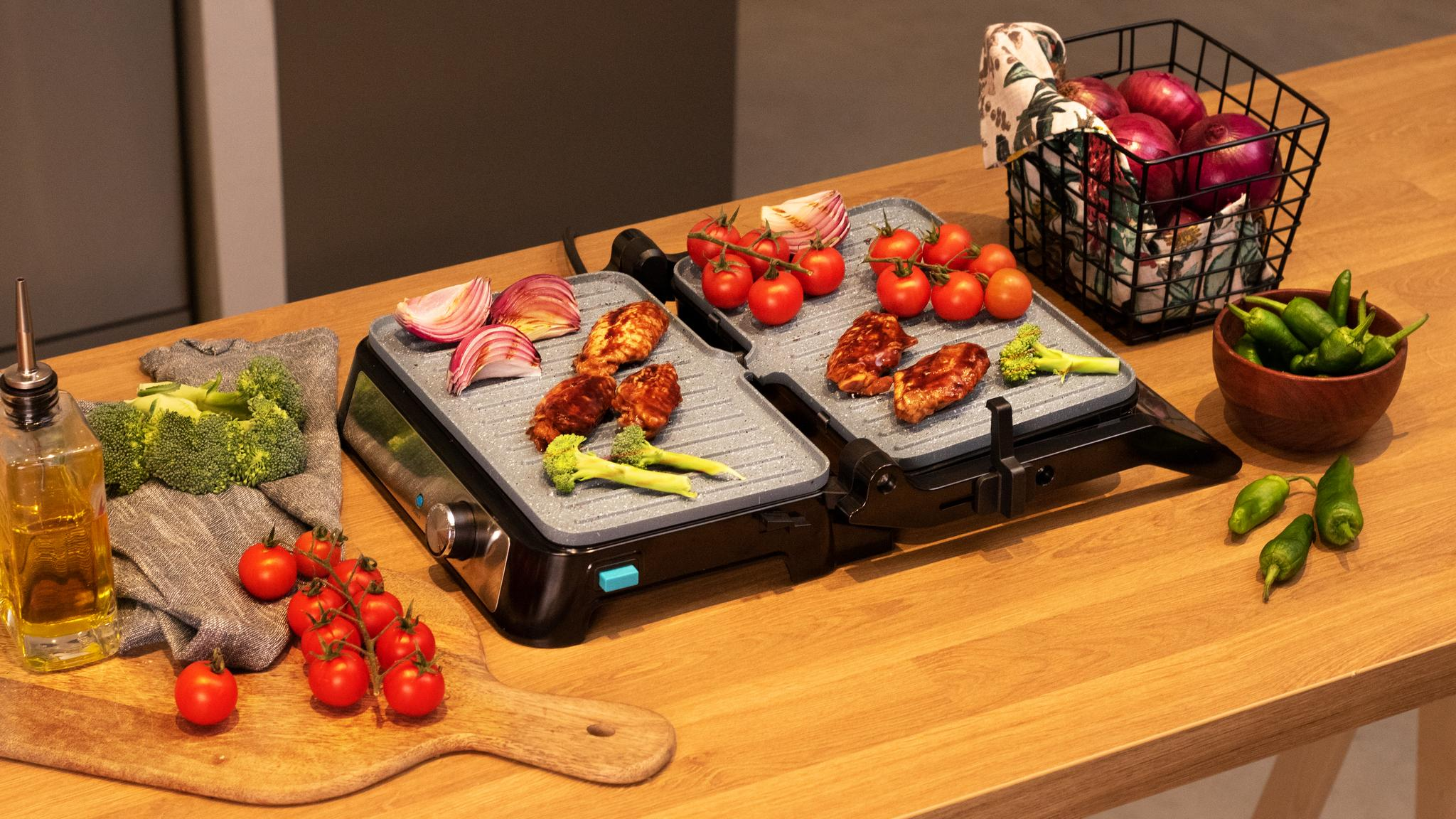 Parrilla con comida, tomates, cebollas y una cesta de verduras.
