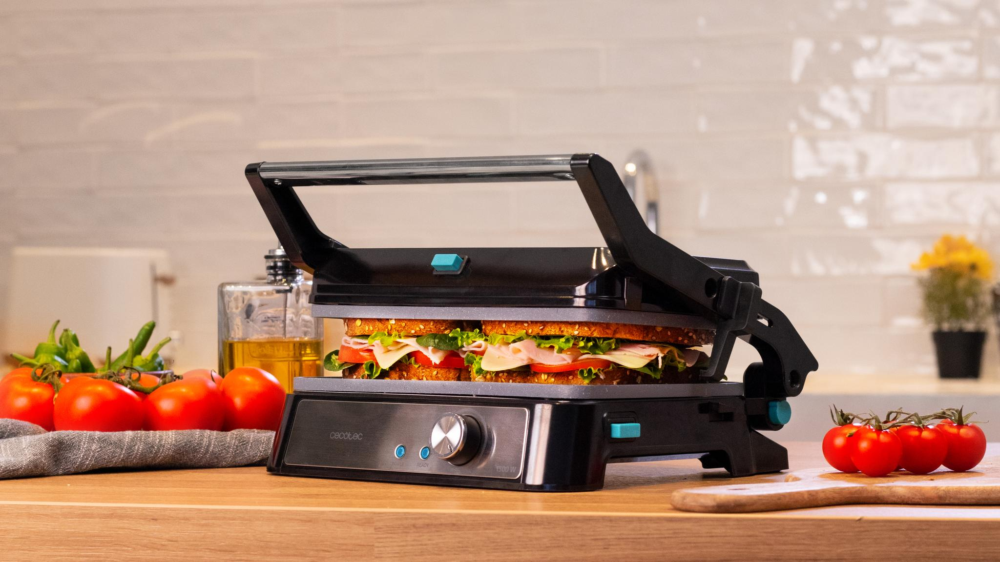Prensa para sándwiches con sándwich dentro, tomates y otros ingredientes en la mesa.