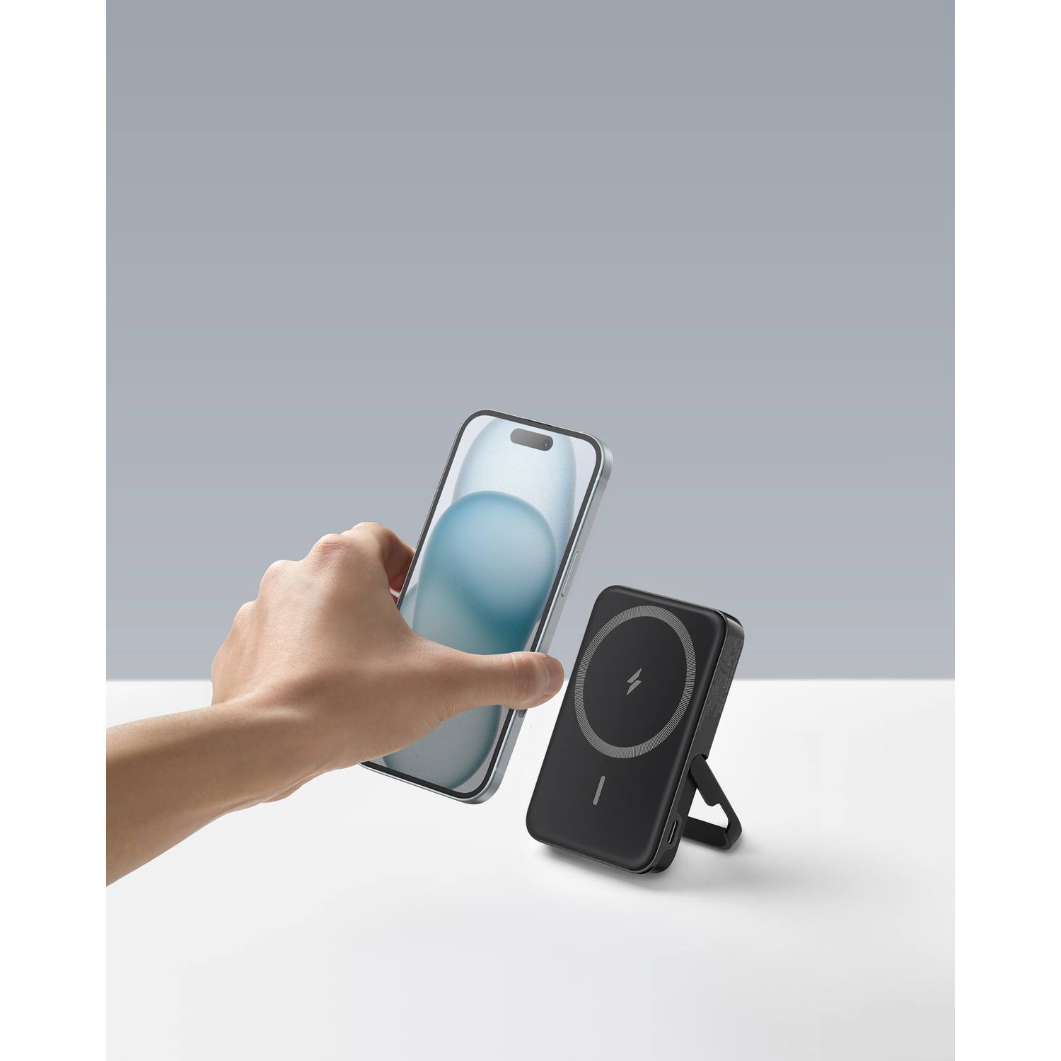A hand holding a smartphone next to a black wireless charger.