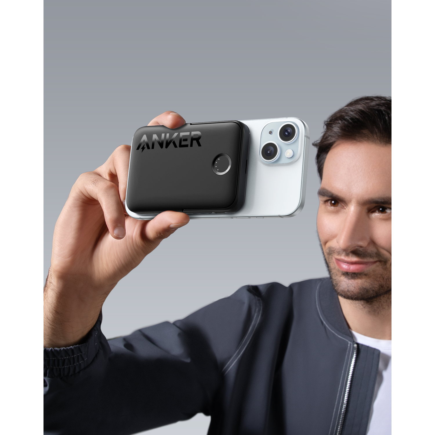 A man holding a black Anker charger attached to a white iPhone. A close-up shot.