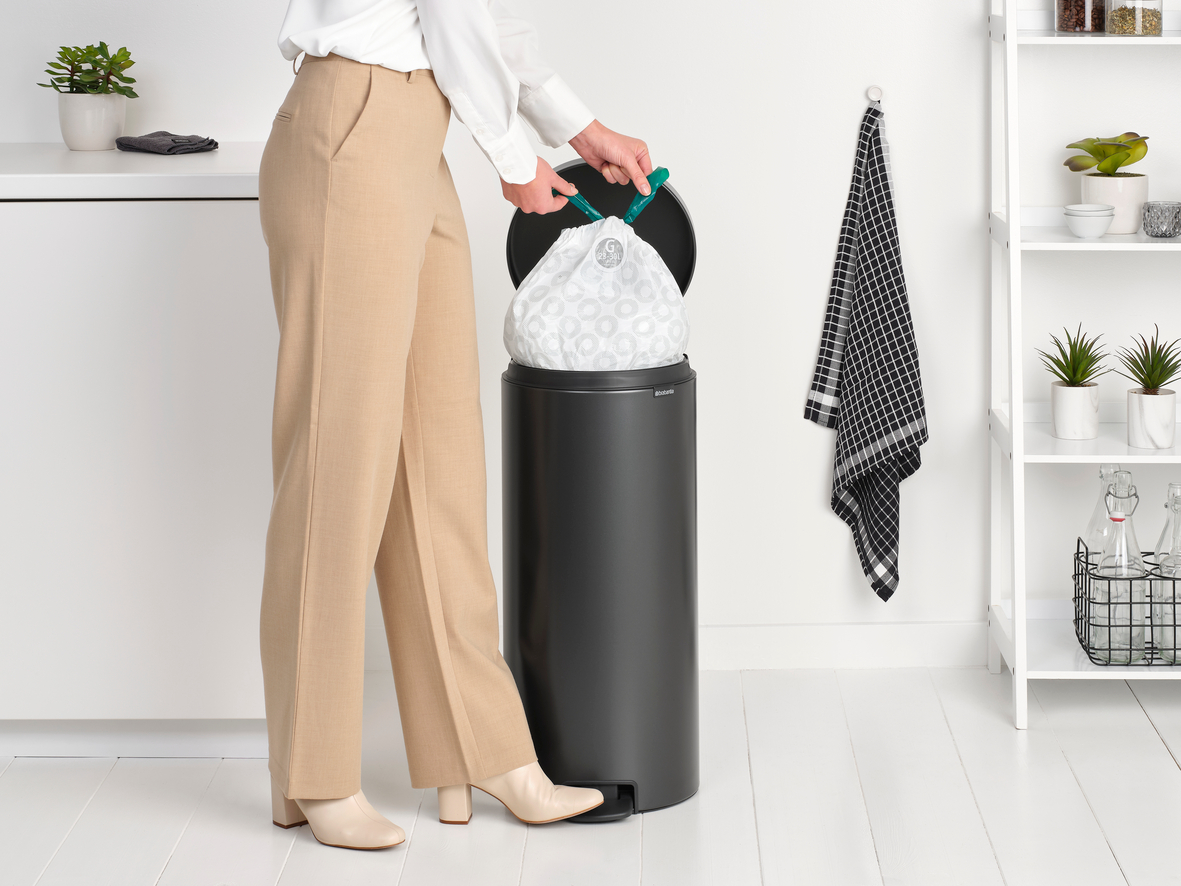 Frau, die einen Müllsack in einen schwarzen Mülleimer legt.