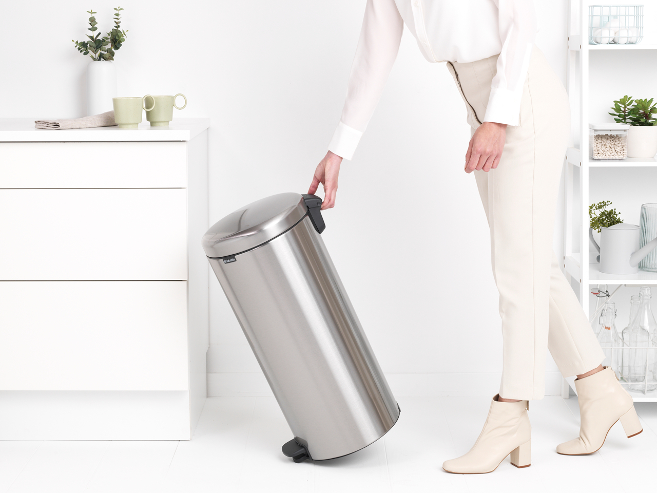 Eine Frau hält einen silbernen Mülleimer. Der Behälter ist zylindrisch mit Fußpedal und Deckel.
