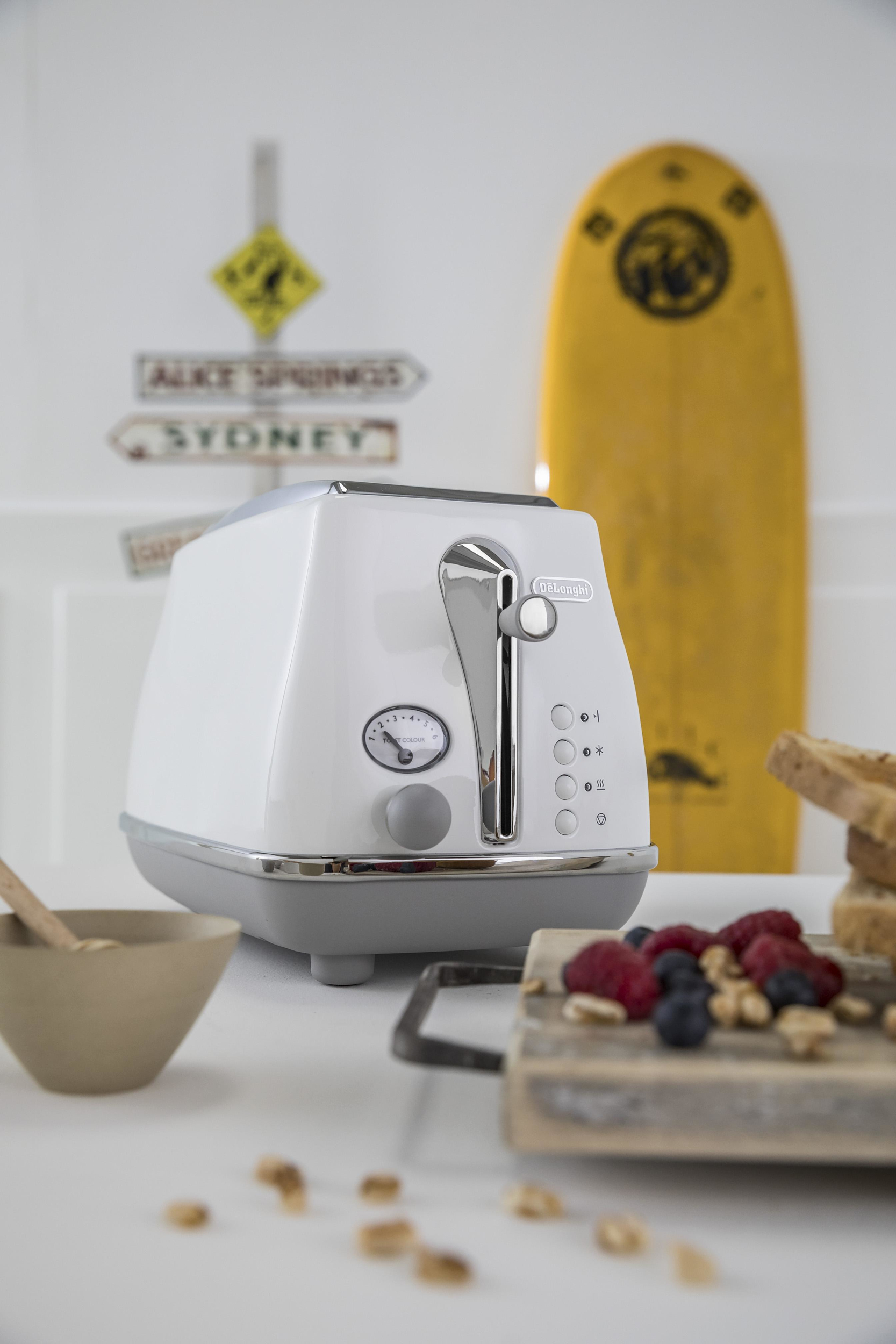 Biały toster na białej powierzchni. Deska surfingowa i znaki w tle. Jedzenie i miska.